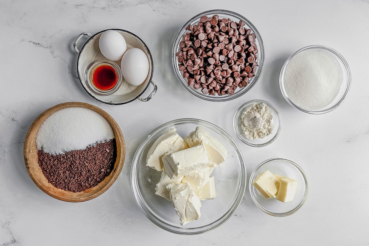 Ingredients for Taste Recipes chocolate cheesecake in bowls on a marble surface.