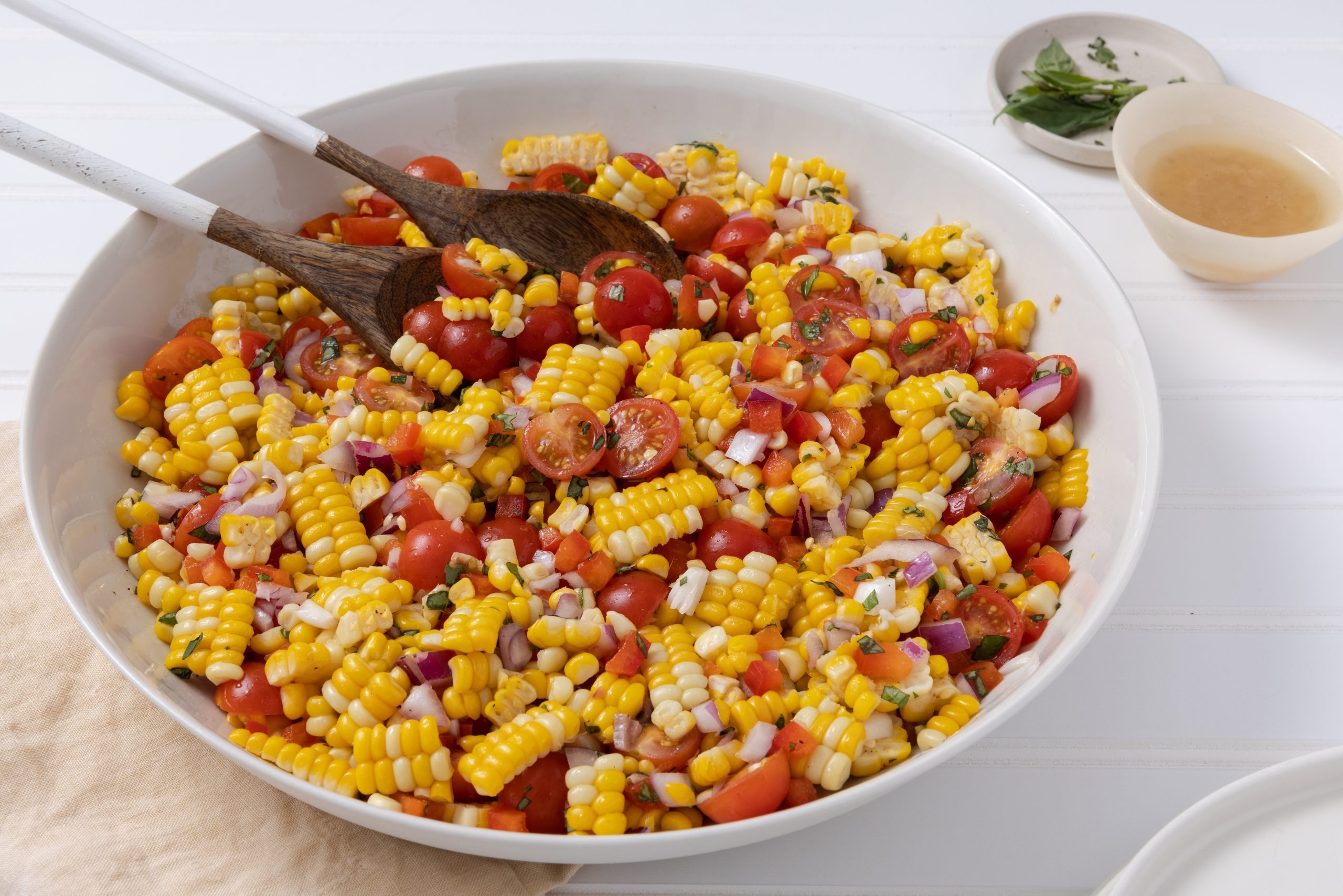 Salad served in large ceramic dish with salad dressing on the side and serving wooden spoons.