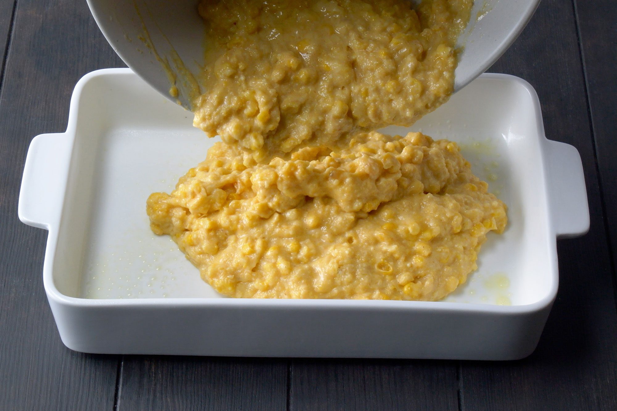 Pouring Cornbread Casserole mixture into a greased baking dish