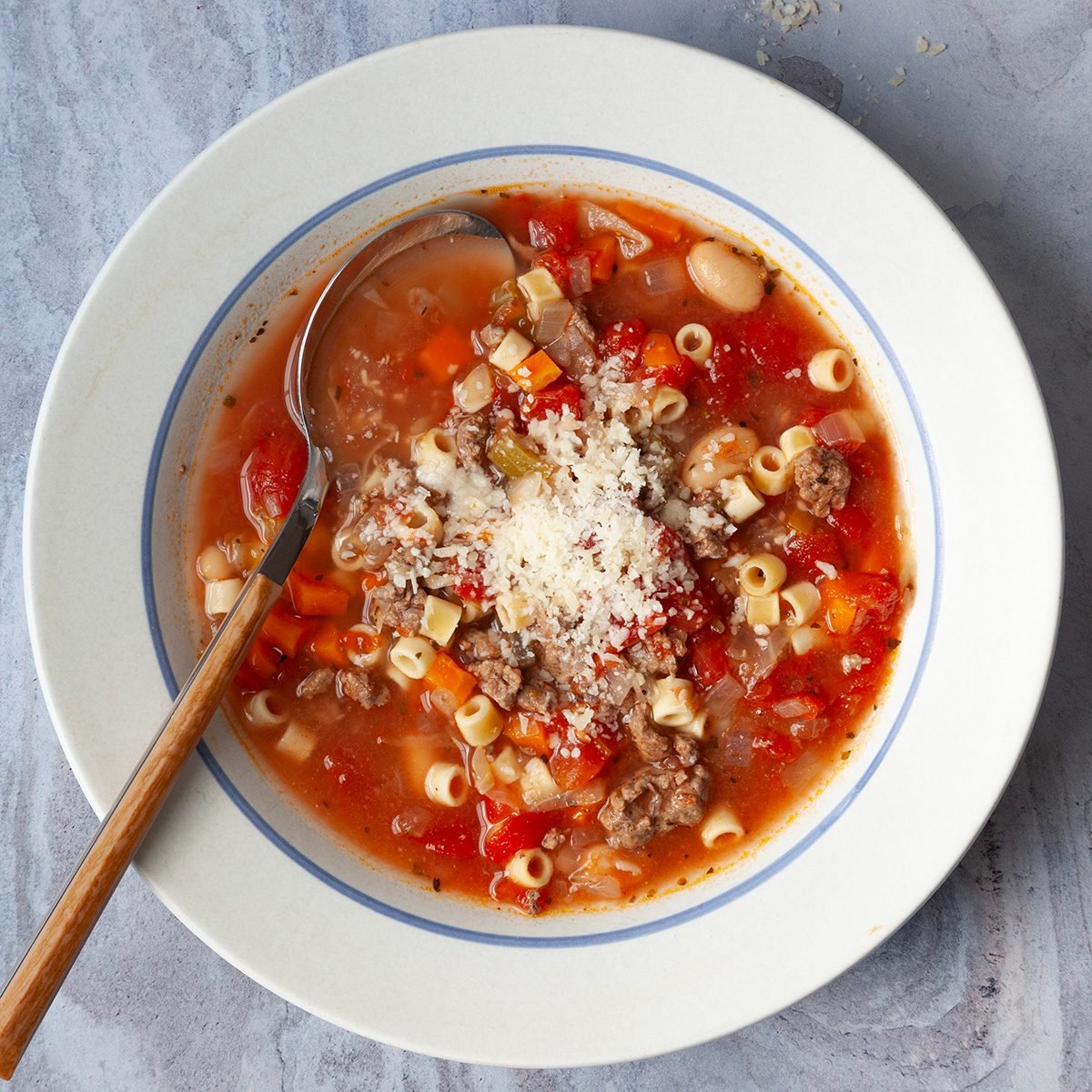 Single servings of Taste of Home Crockpot Pasta Fagioli is white bowls on blue gray surface with small bowl of parmesan cheese