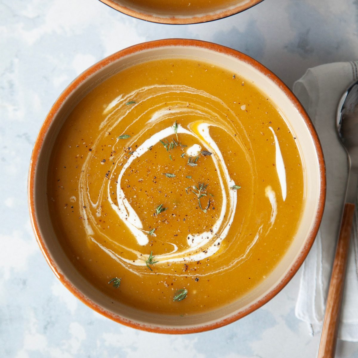 two single servings of butternut squash soup with a sour cream and fresh thyme garnish