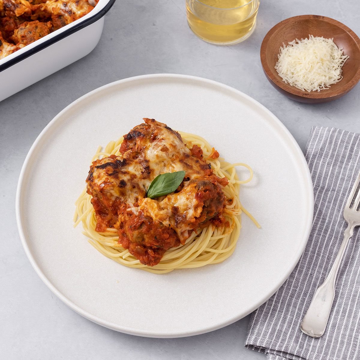 Baked meatballs served with spaghetti on a plate and baking dish on the side.