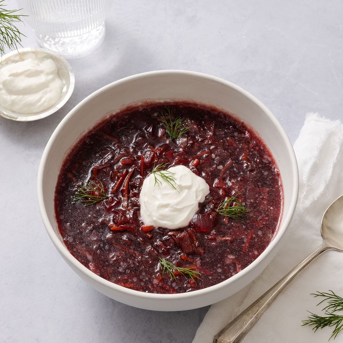 Borscht soup served in ceramic bowl garnisehd with sour cream and dill sprigs.