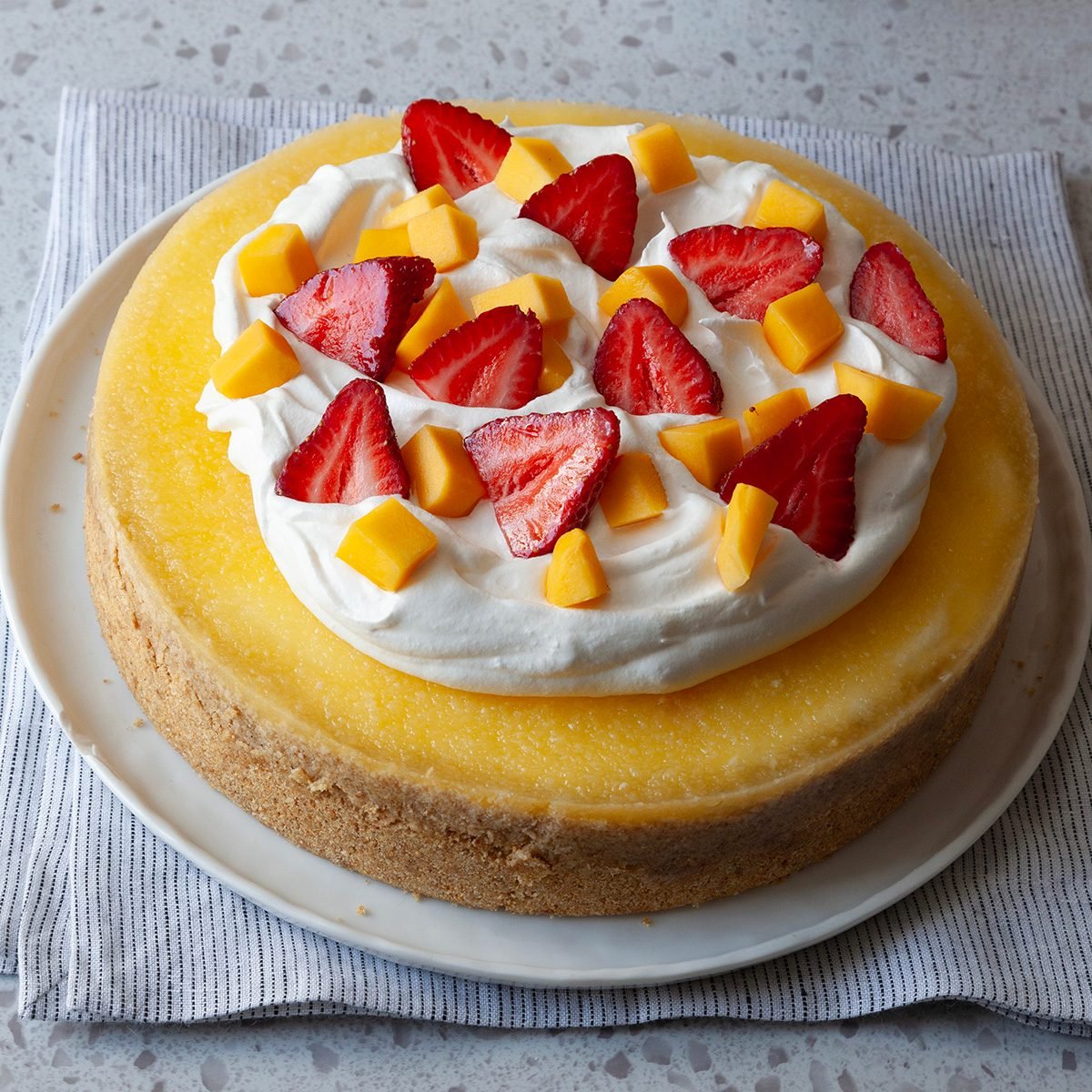 Full yield of Taste of Home Mango Cheesecake garnished with whipped cream, strawberries and mangoes