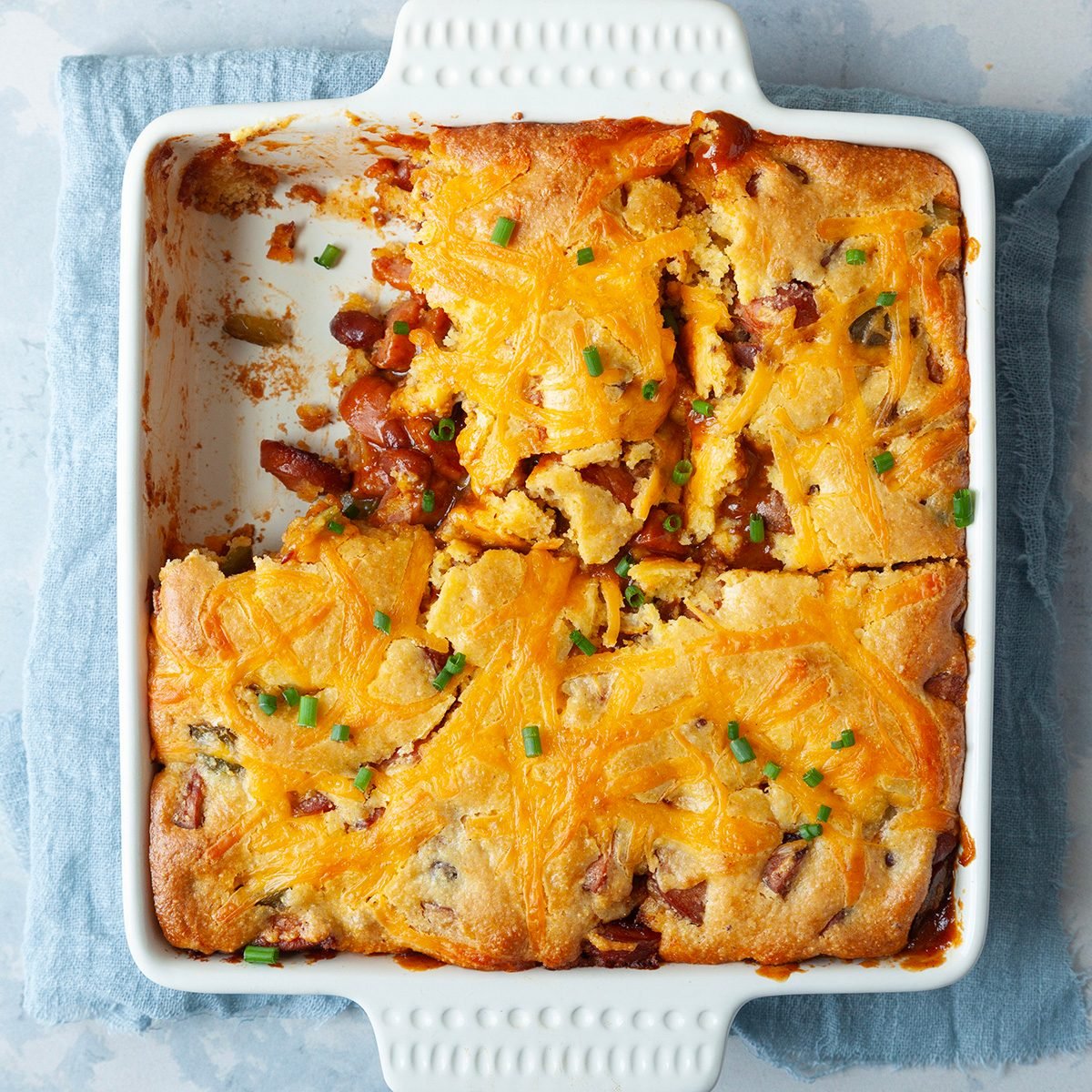 overhead angle of full yield of Chili Cheese Dog Casserole in an white 8-inch baking dish with a blue linen