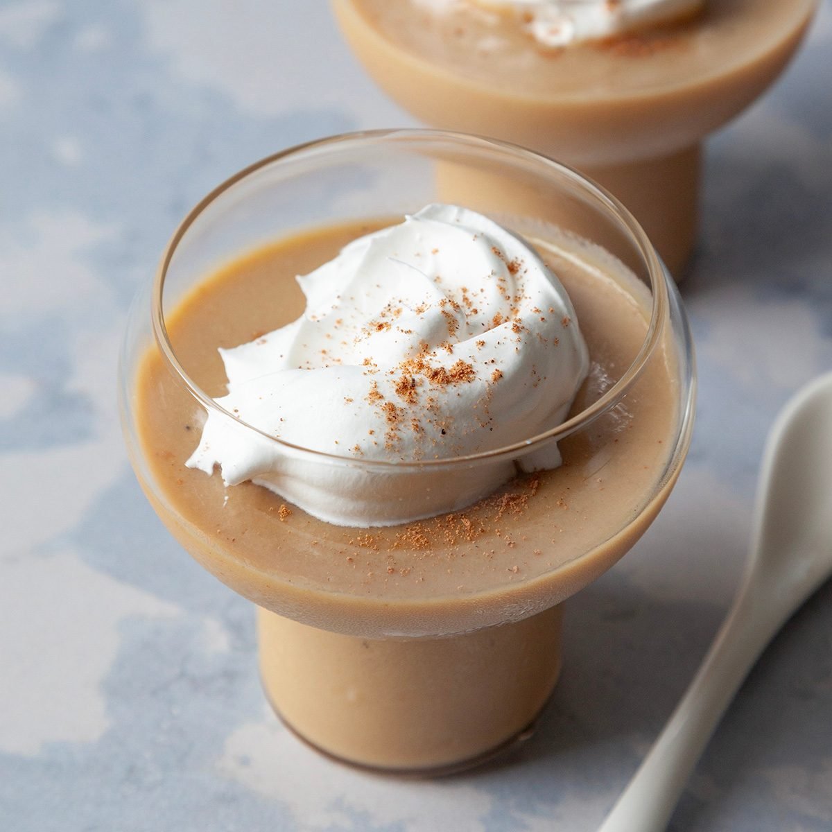 Two single servings of Butterscoth pudding with whipped cream and ground nutmeg in dessert dishes with white spoons