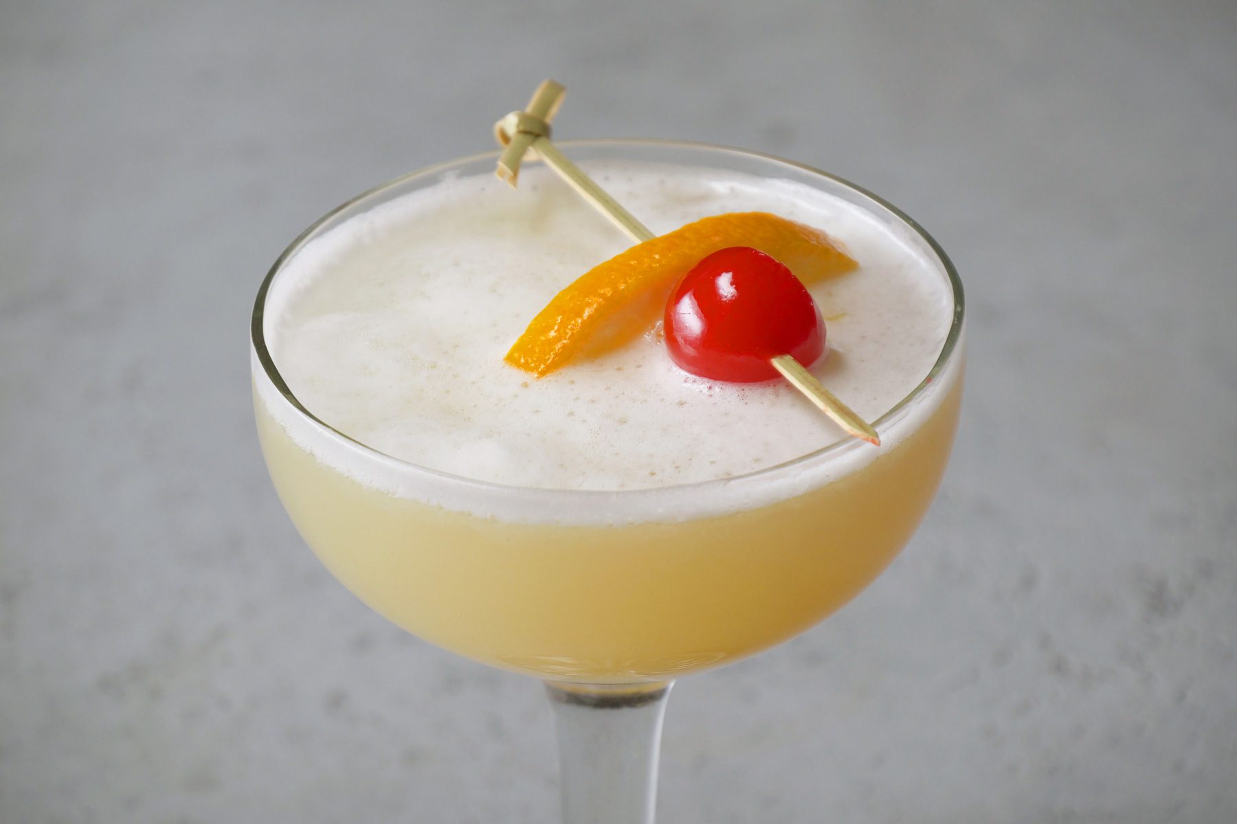 A close-up shot of Whiskey Sour in a cocktail glass garnished with cherry