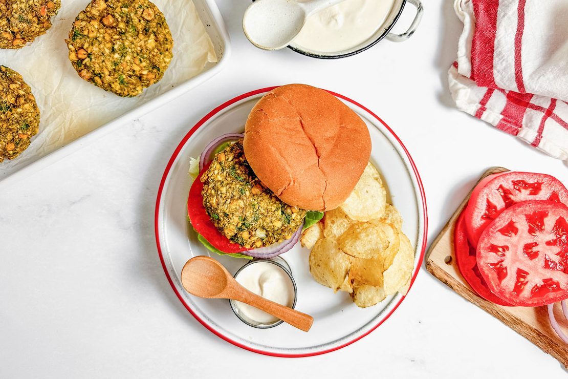 Taste of Home Falafel Burgers with tahini yogurt sauce on an enamel plate with potato chips.