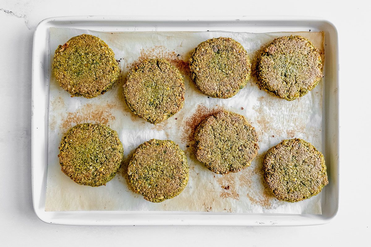 Taste of Home falafel burgers on a parchment lined baking sheet on a marble surface.