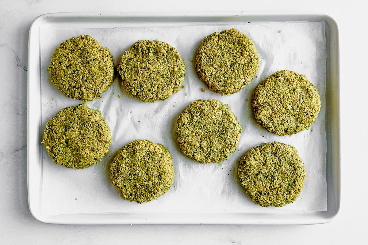 Unbaked Taste of Home Falafel Burgers on a parchment lined baking sheet on a marble surface.