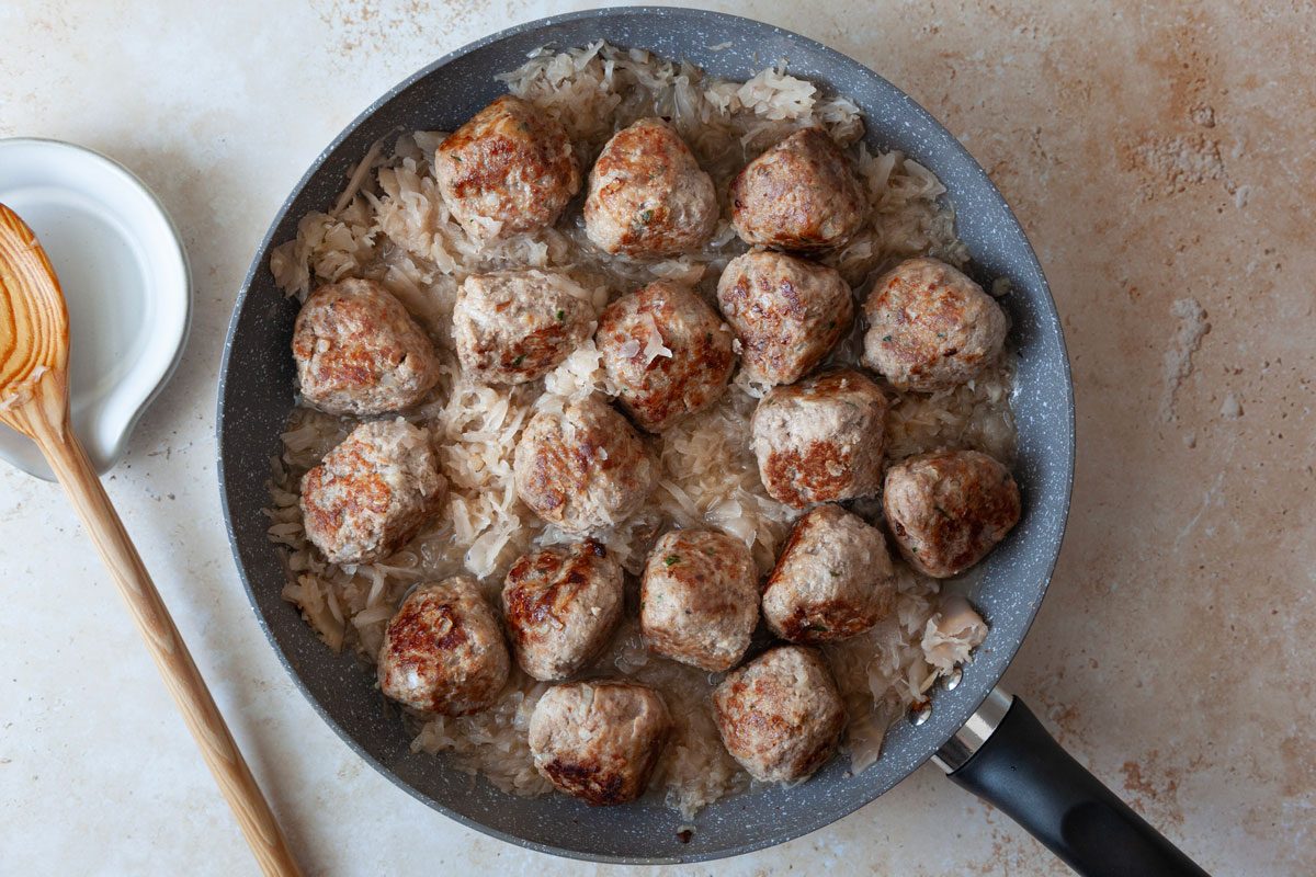 Taste of Home German Meatballs in a dark gray pan on a tan surface with a wooden spoon in a white spoon rest