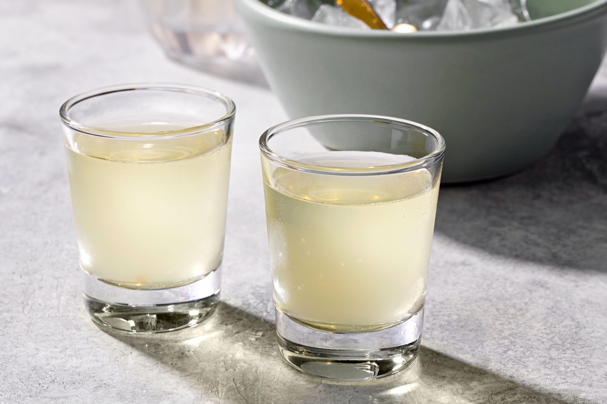 Table view shot of Green Tea Shots; served in glasses; shaker; ice cubes bowl; marble background;