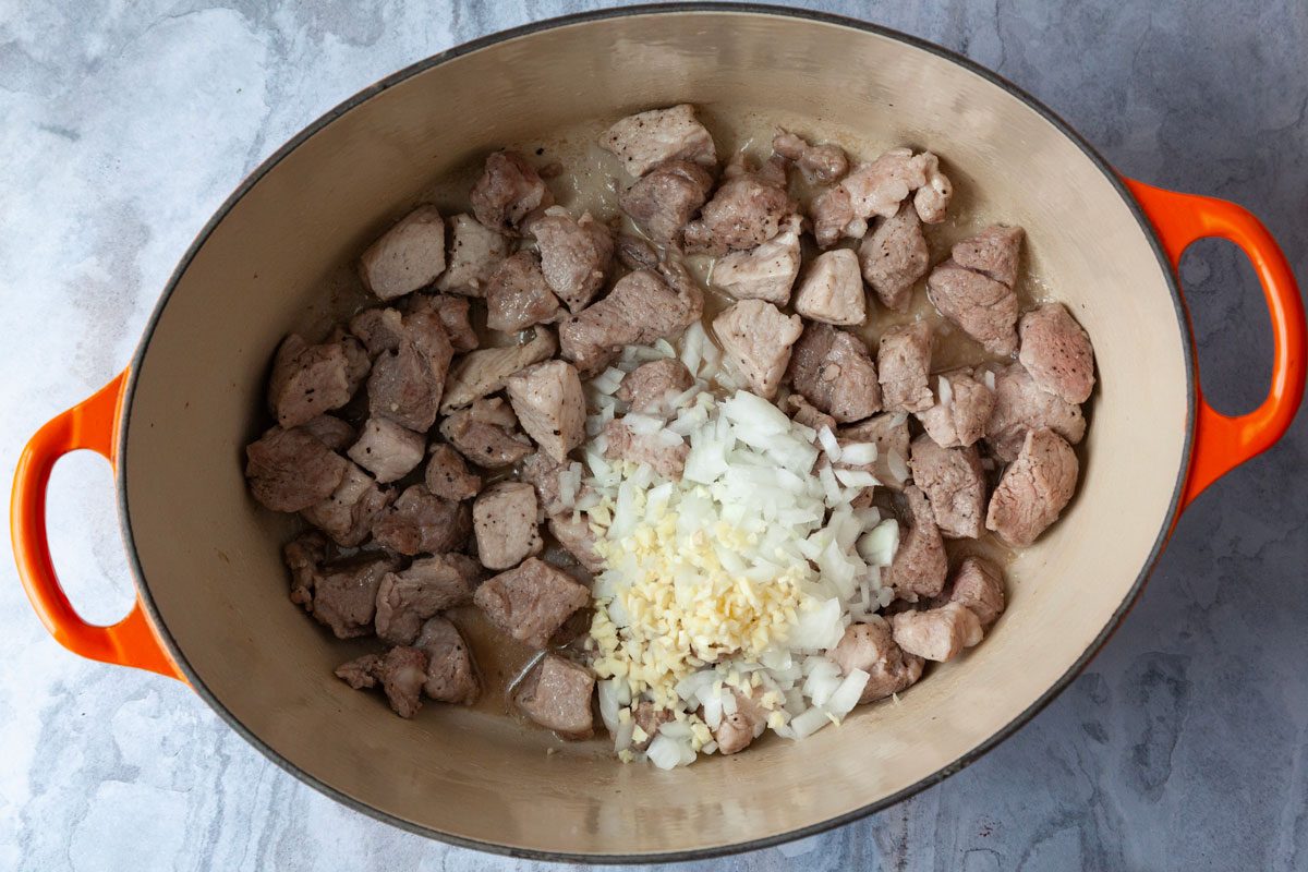 Step 1 of Taste of Home Green Chile Pork Stew is to brown the meat in oil and add the onion and garlic