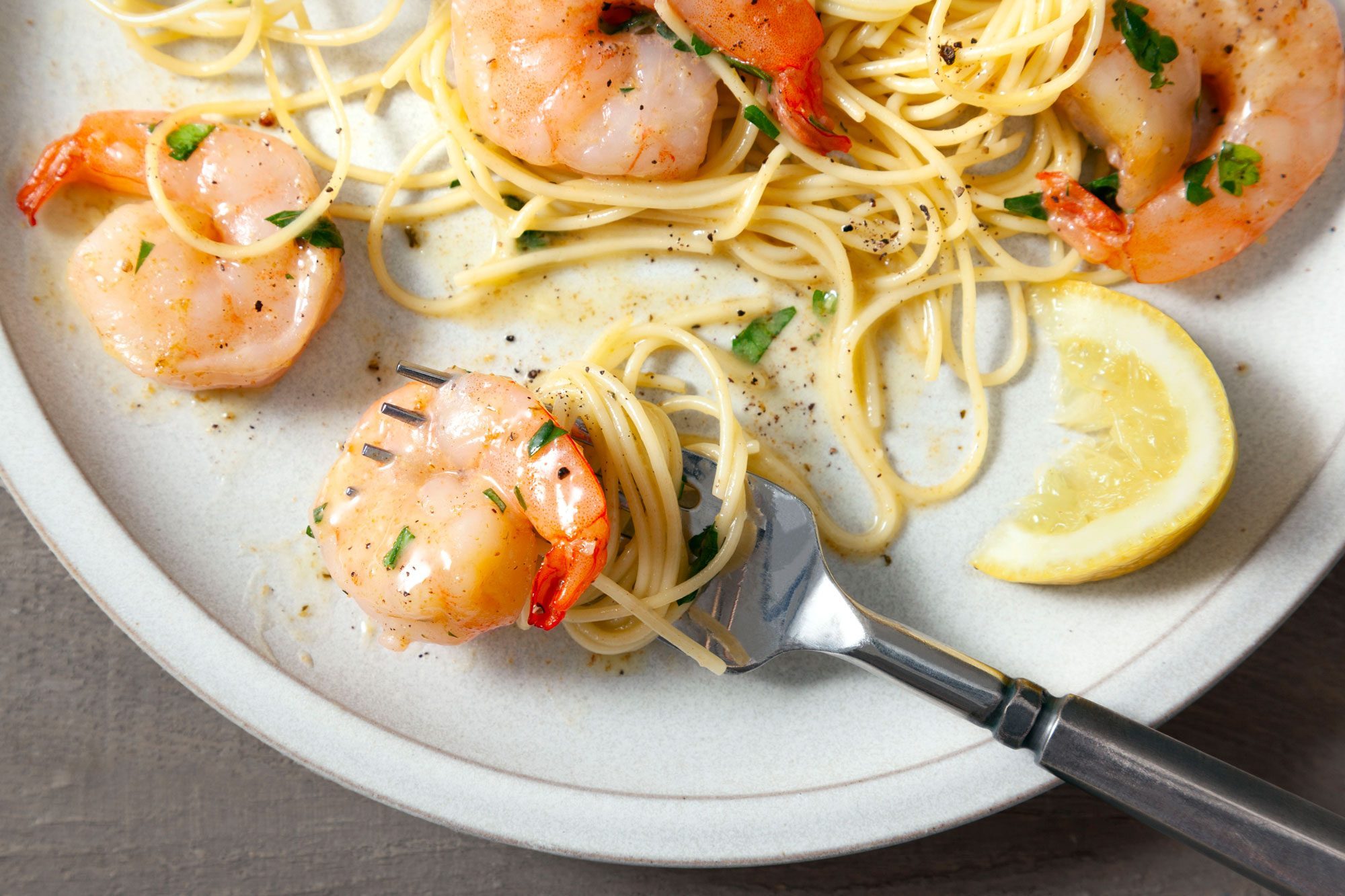 Close shot of Garlic Lemon Shrimp; served in white plate with pasta and lemon wedges; fork; wooden background;