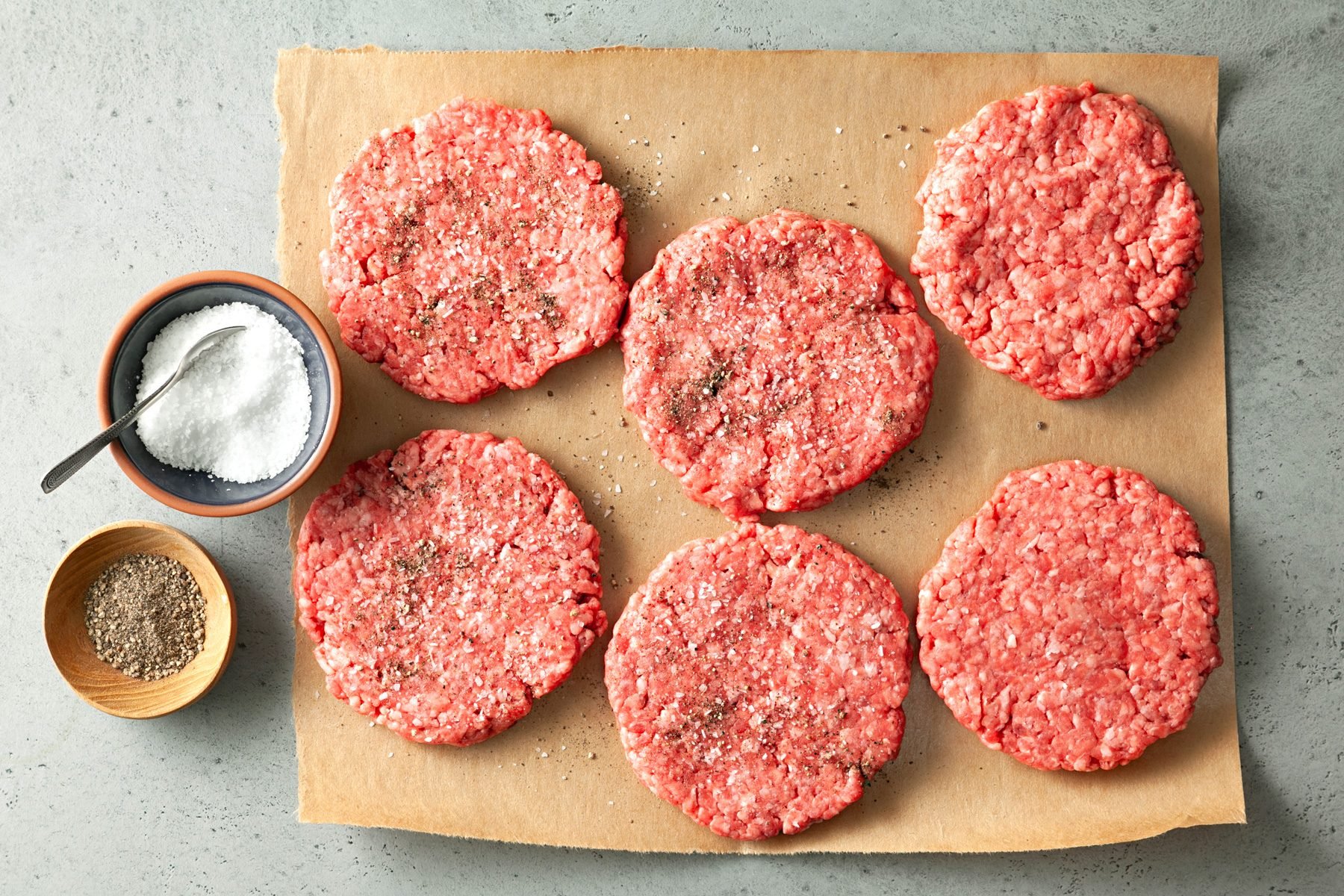 Top view of six beef patties. Sprinkled each side with salt and pepper.