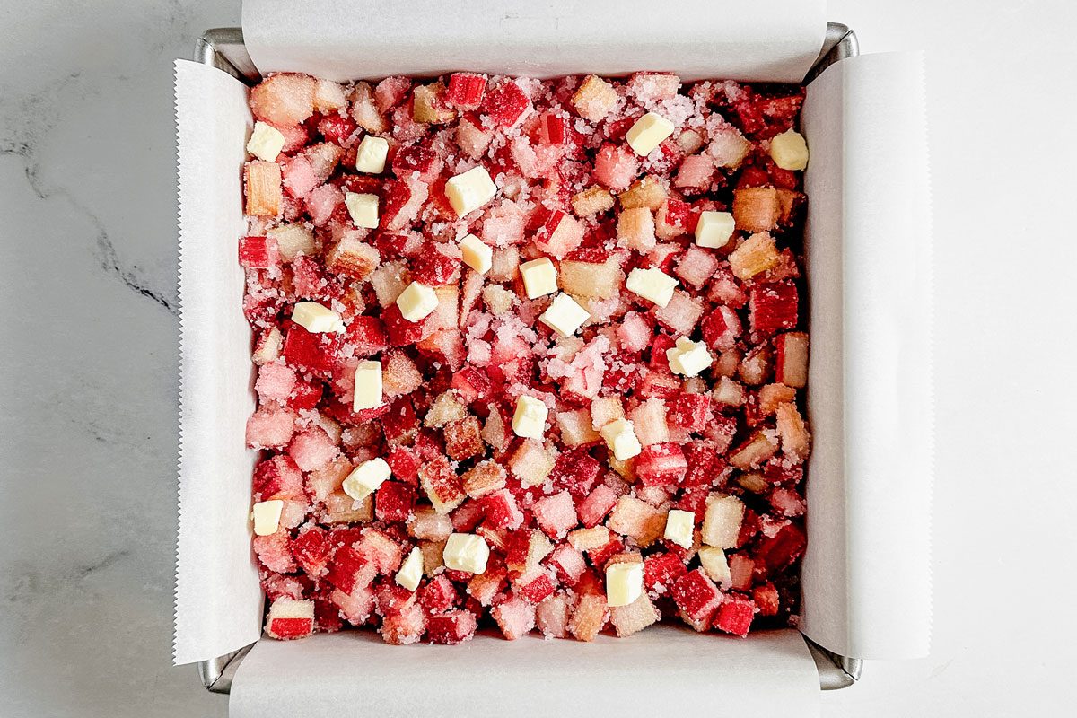 Rhubarb butter and sugar in a metal baking pan for Taste Recipes rhubarb cobbler.