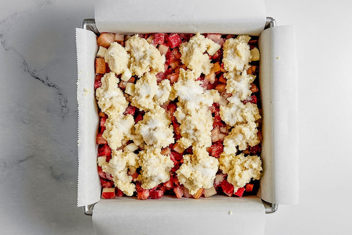 Unbaked Taste of Home rhubarb cobbler in a square metal baking pan on a marble surface.