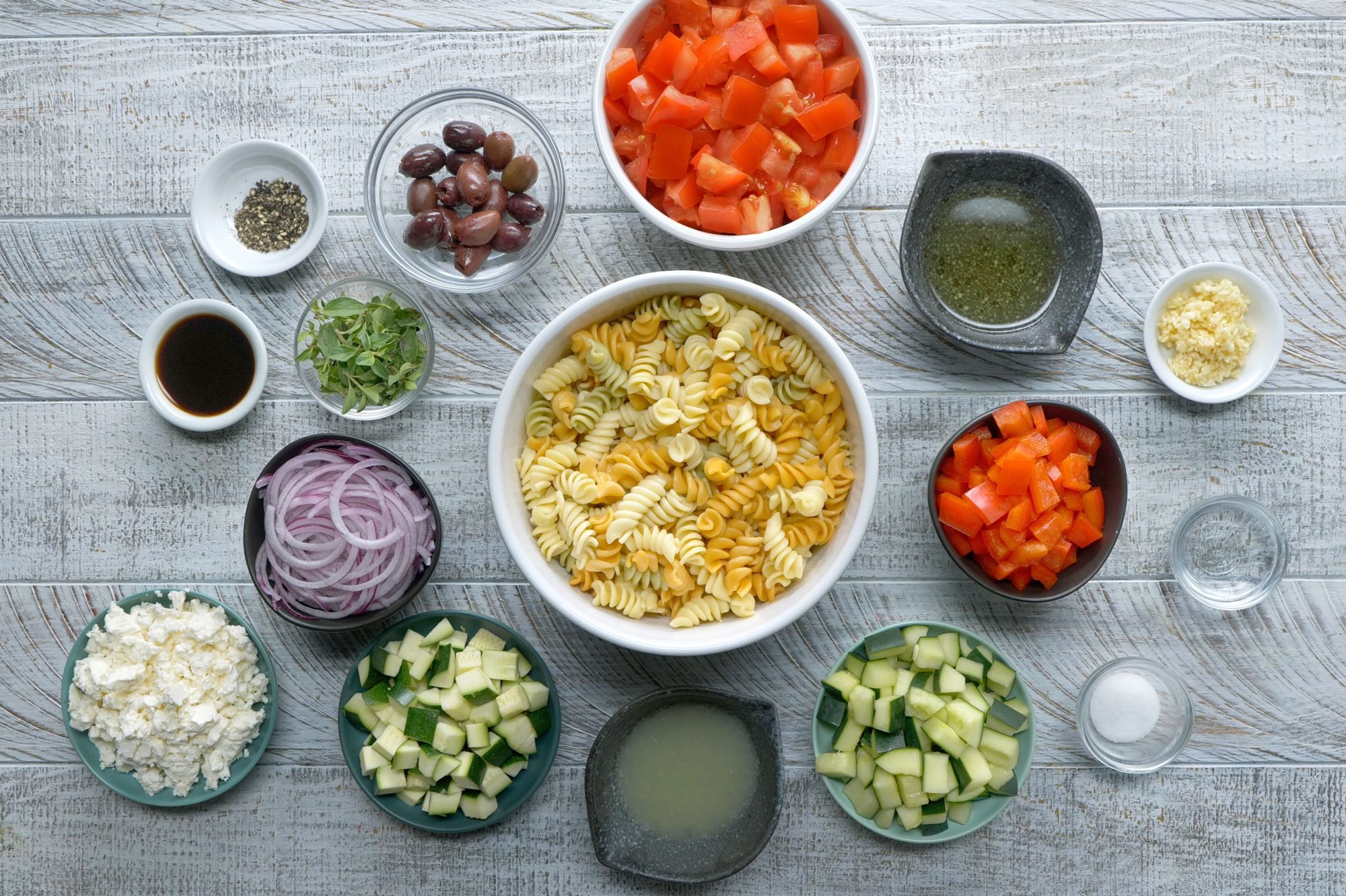 overhead shot of all ingredients for Rotini Pasta Salad; wooden background;