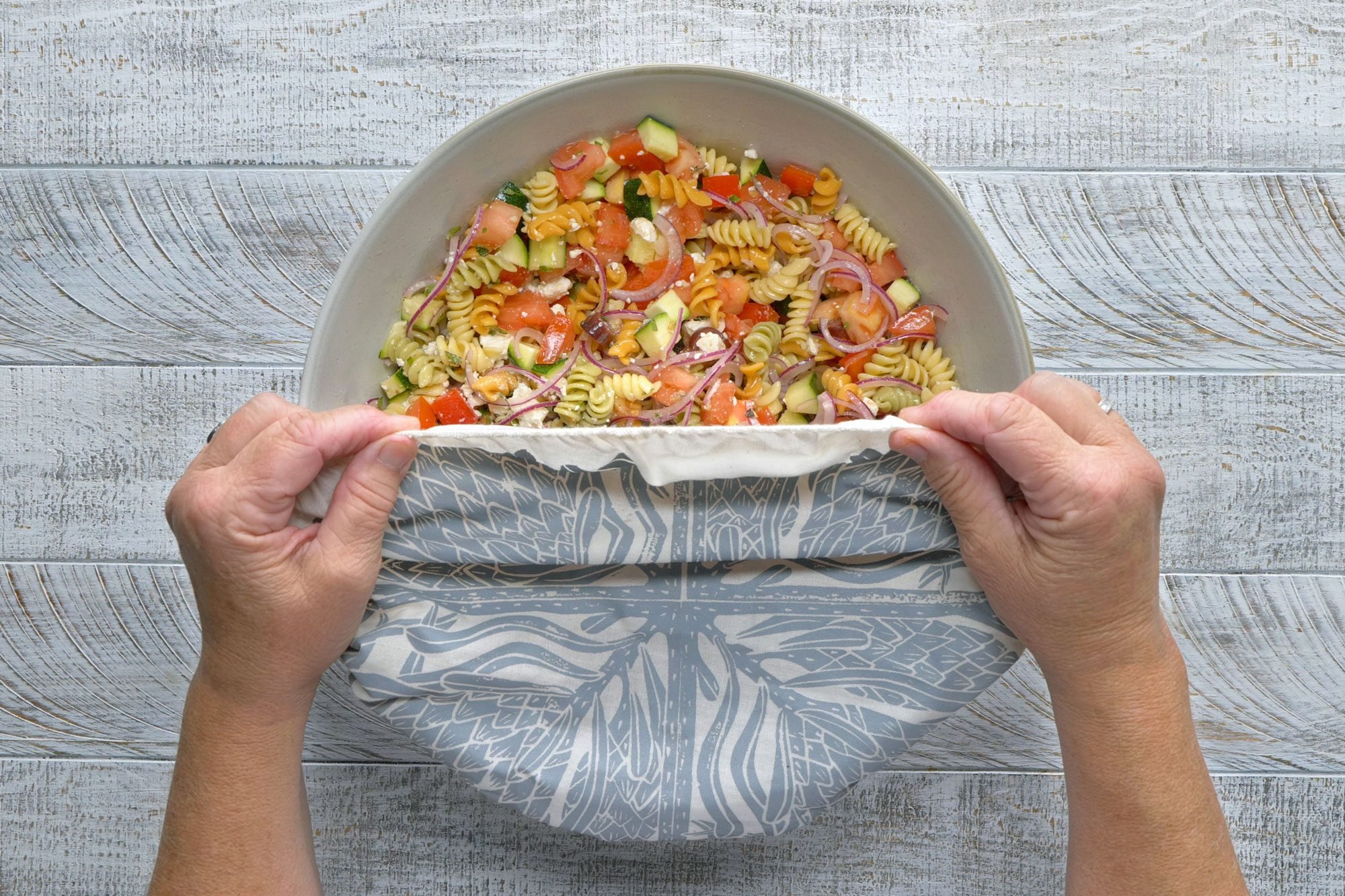 overhead shot of half covered Rotini Pasta Salad; wooden background;