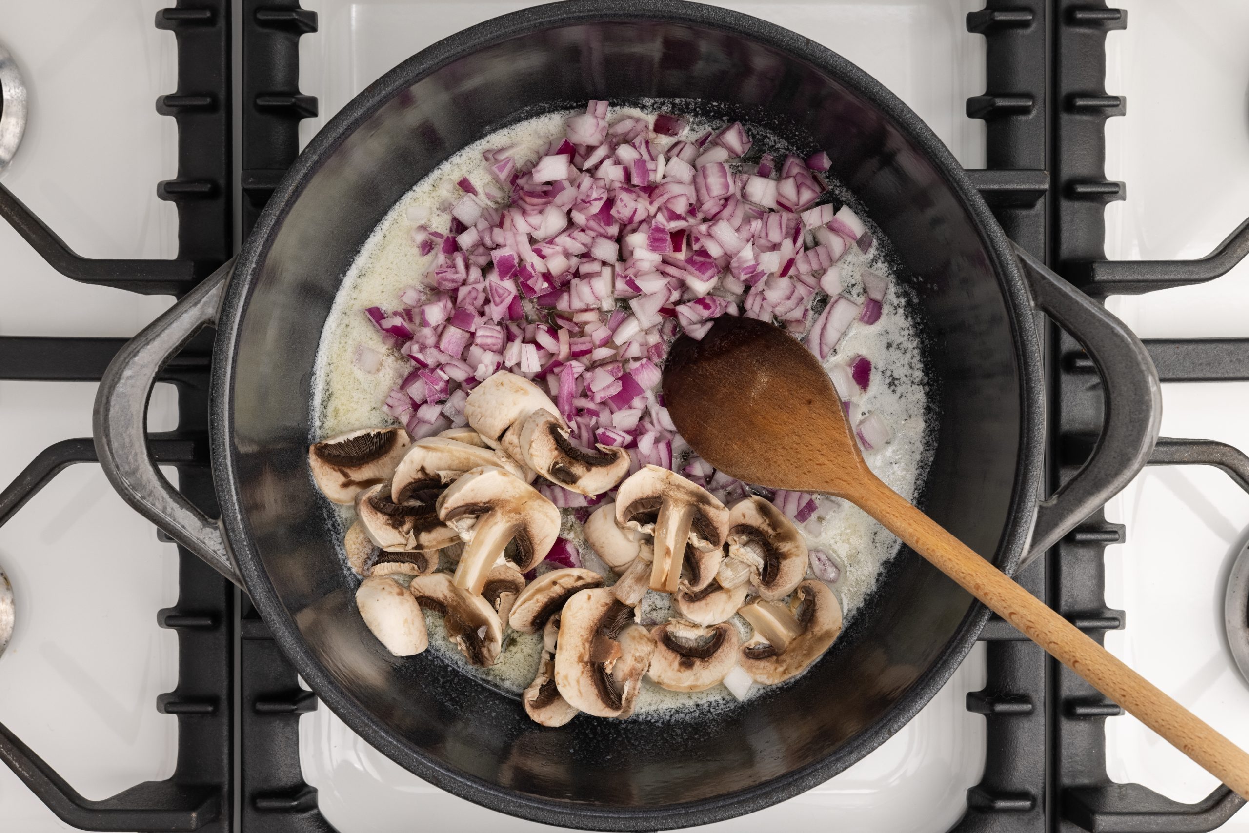 Dutch oven with melted butter, onions and mushrooms on stove top.