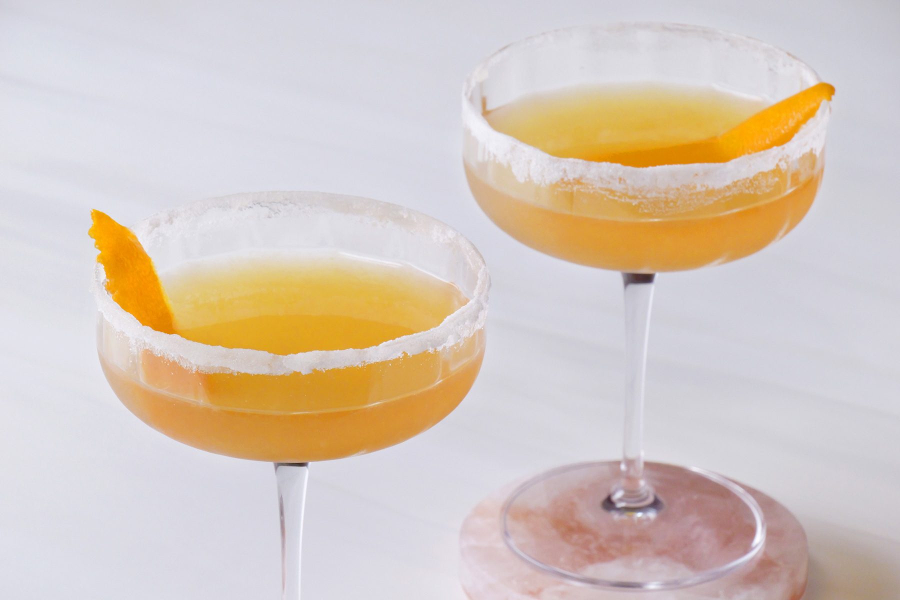 Two glasses of sidecar cocktail with orange peel on a coaster