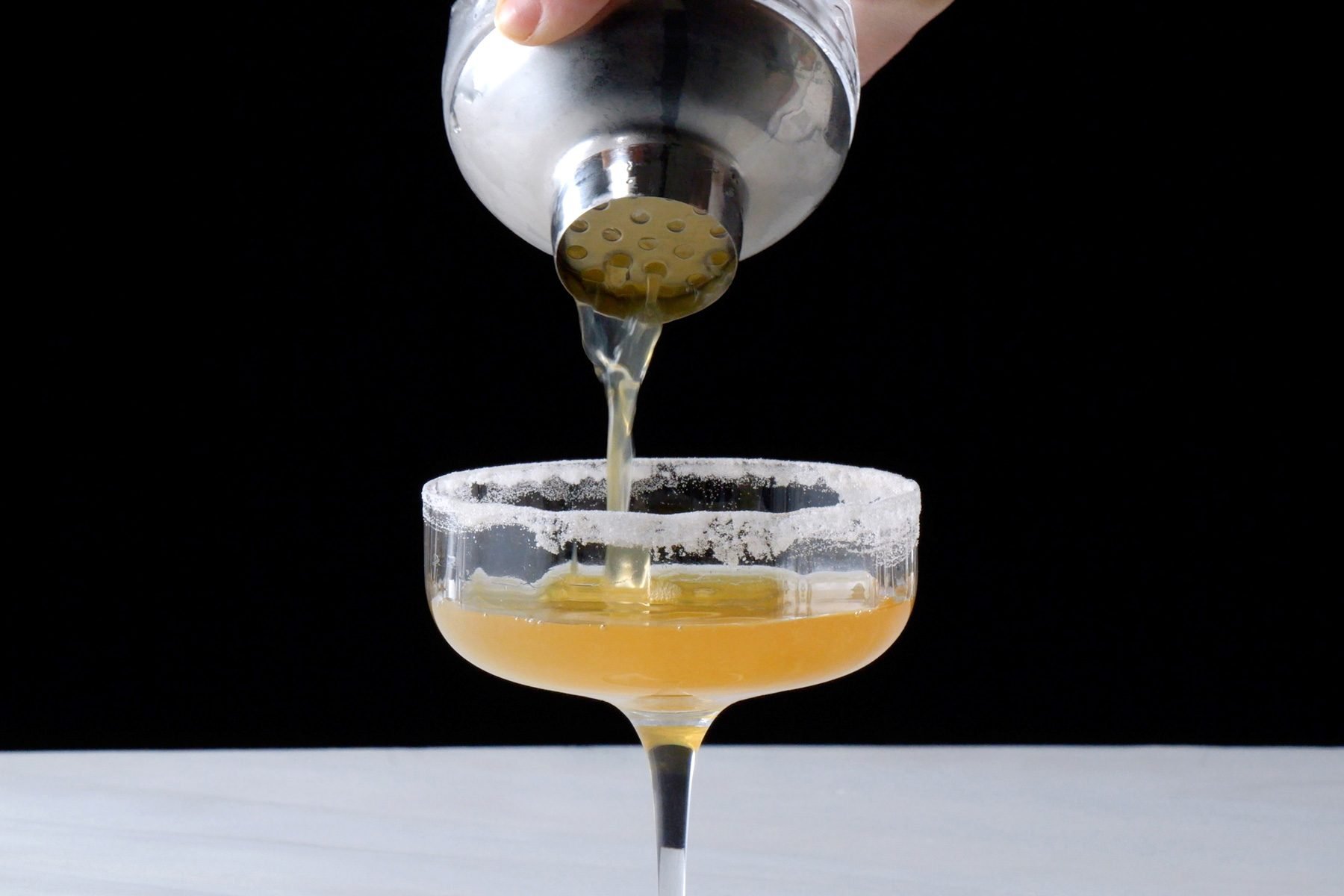 Pouring the cocktail into the coupe glass with sugar on the rim