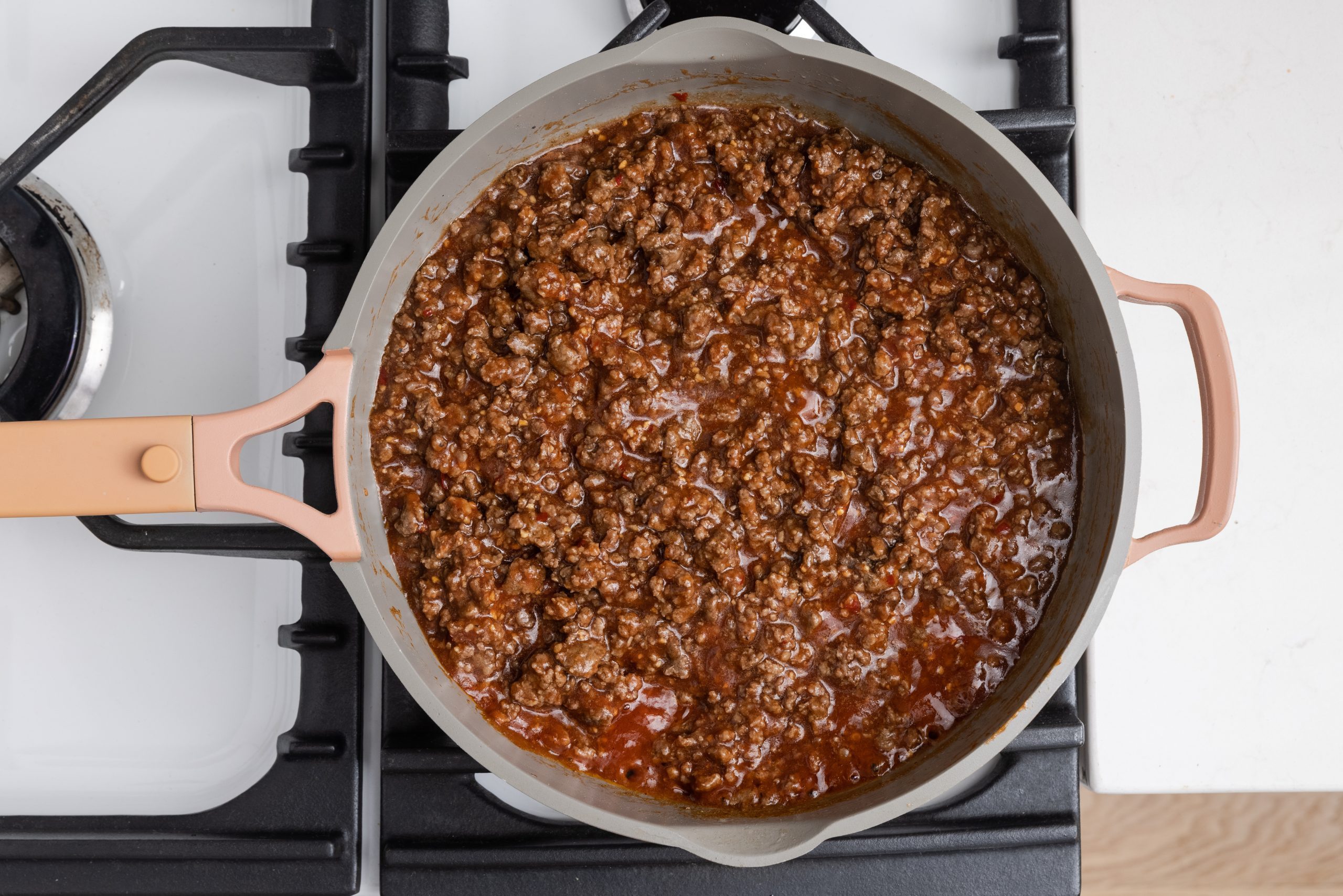 Ground beef being cooked with tomato sauce to make beef mixture.