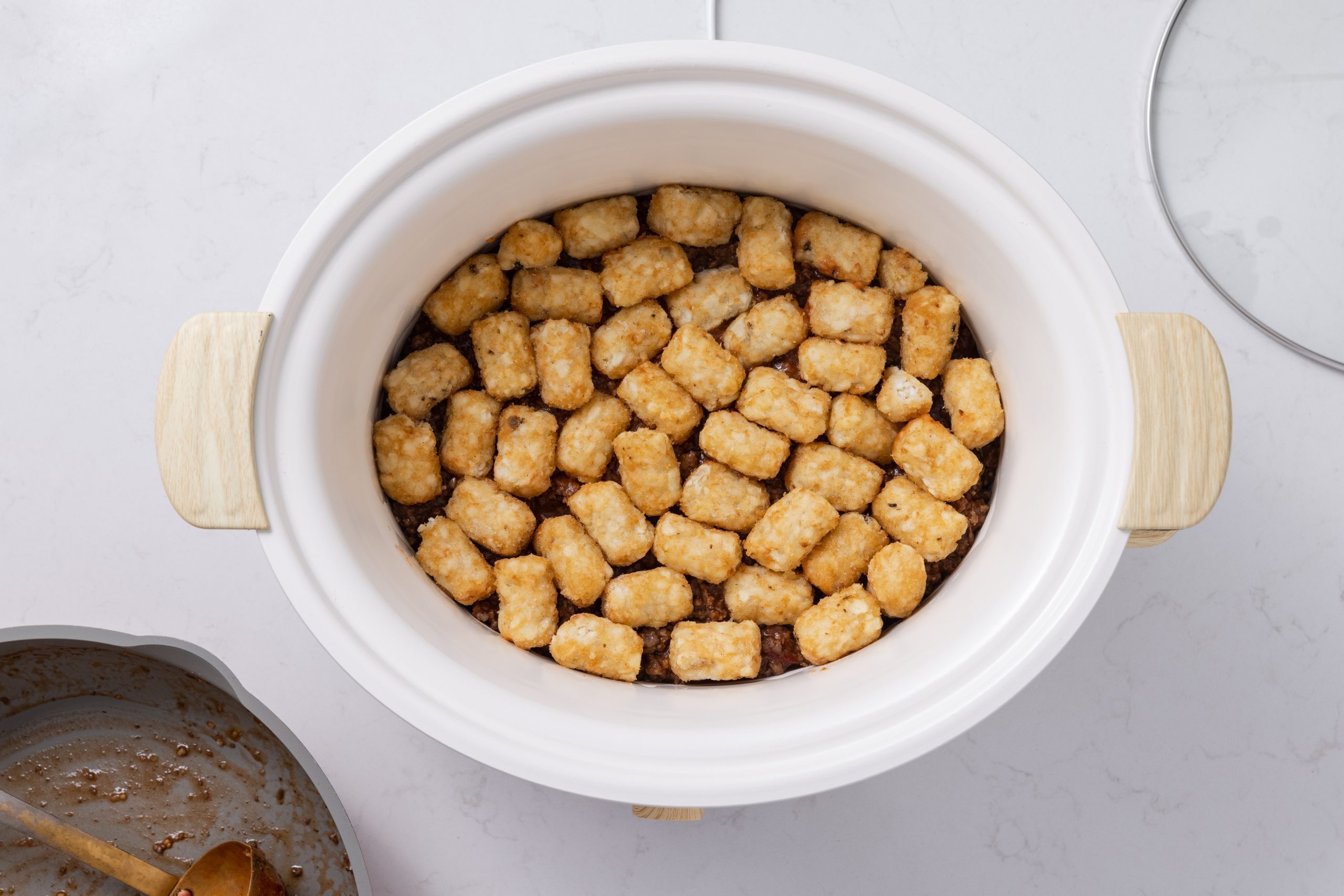 Tater tots and beef mixture piled together in slow cooker.