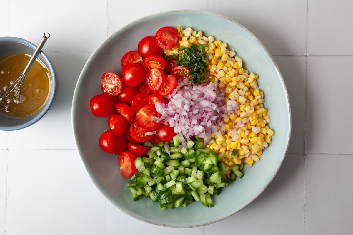 Step 2 of Taste Recipes Summer Corn Salad is to cook the corn in a pan and then combine it with tomatoes, cucumbers, red onion, basil and corn