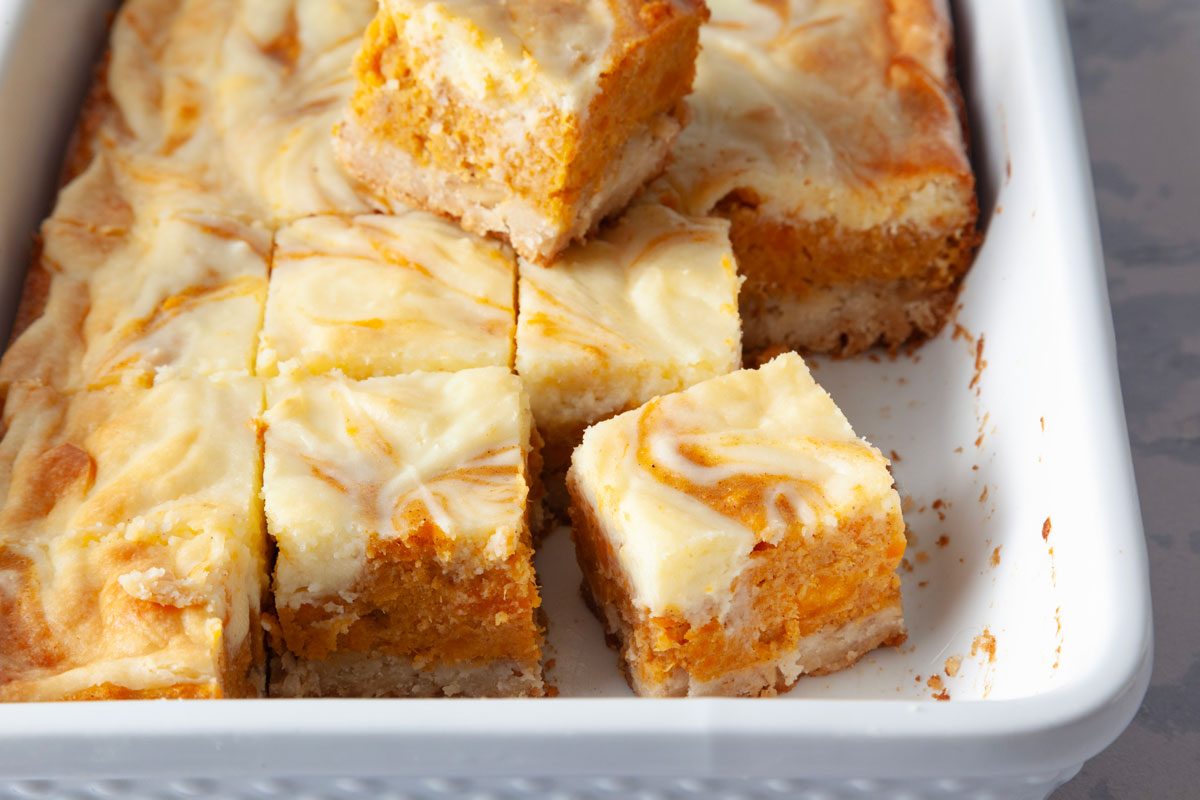 Close up of Taste of Home Sweet Potato Cheesecake Brownies in a white pan, cut into squares