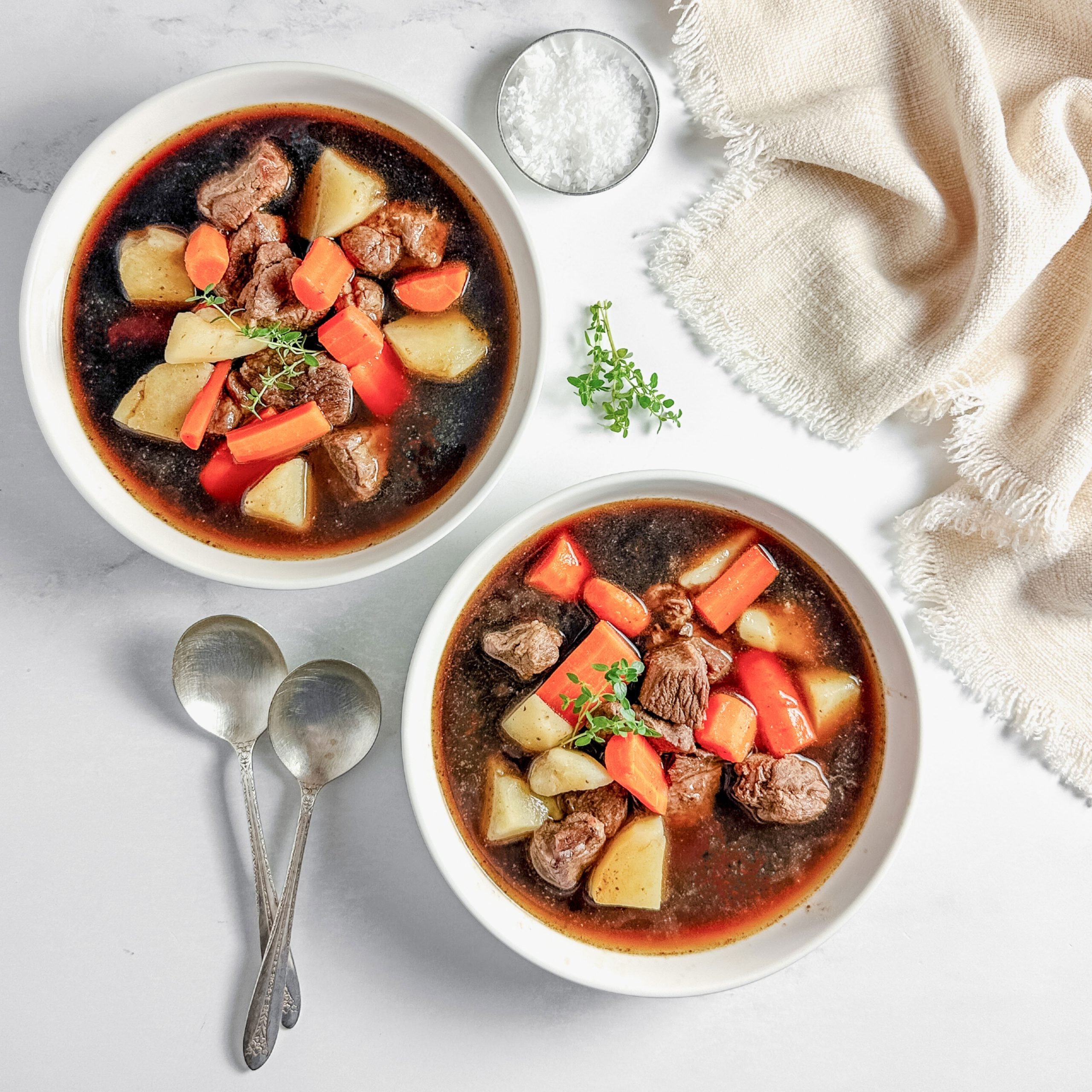 Taste of Home venison stew in white ceramic bowls on a marble surface next to a cloth napkin.