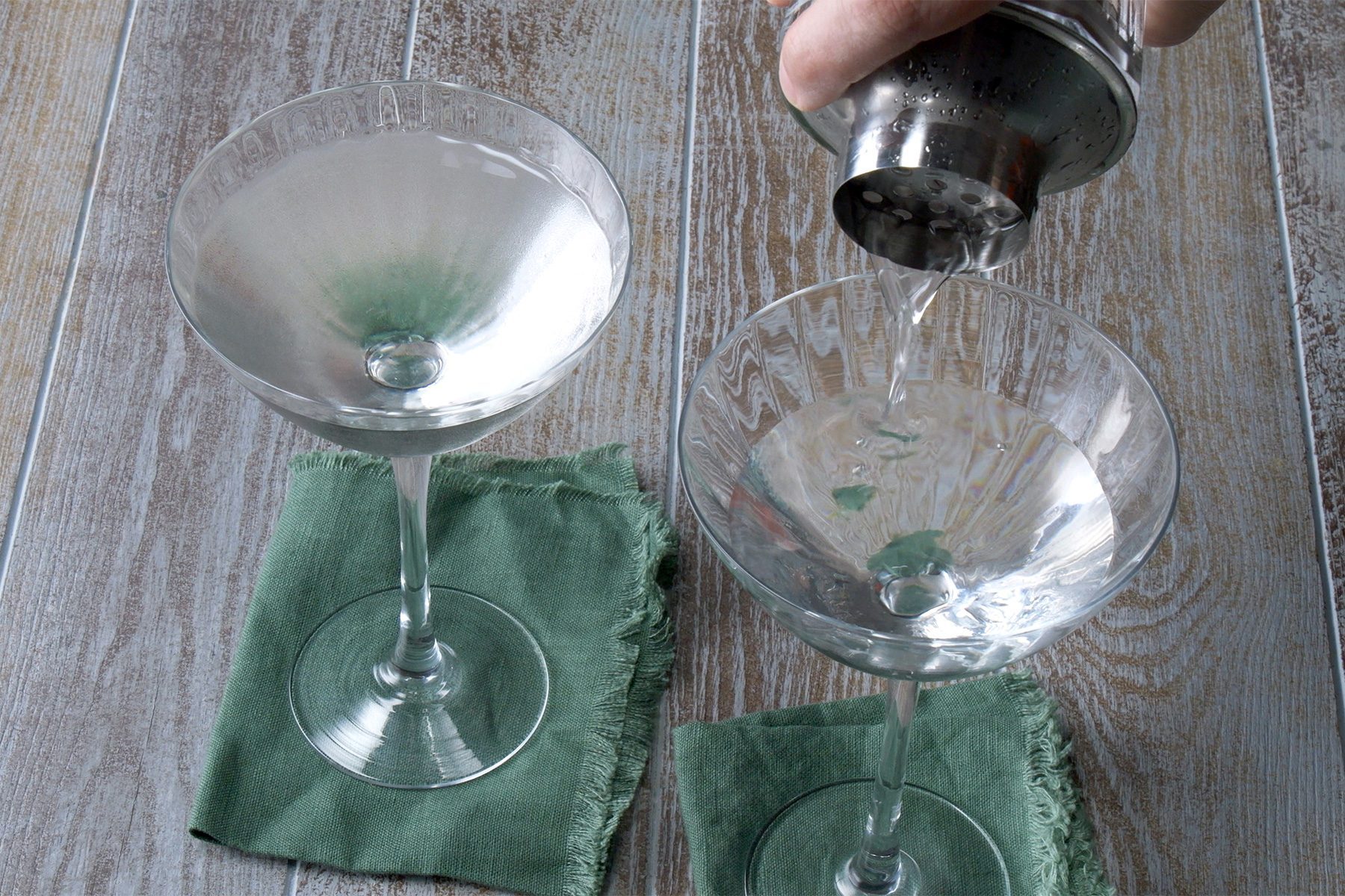 3/4th shot; wooden background; pouring Vesper Martini in martini glasses from shaker;