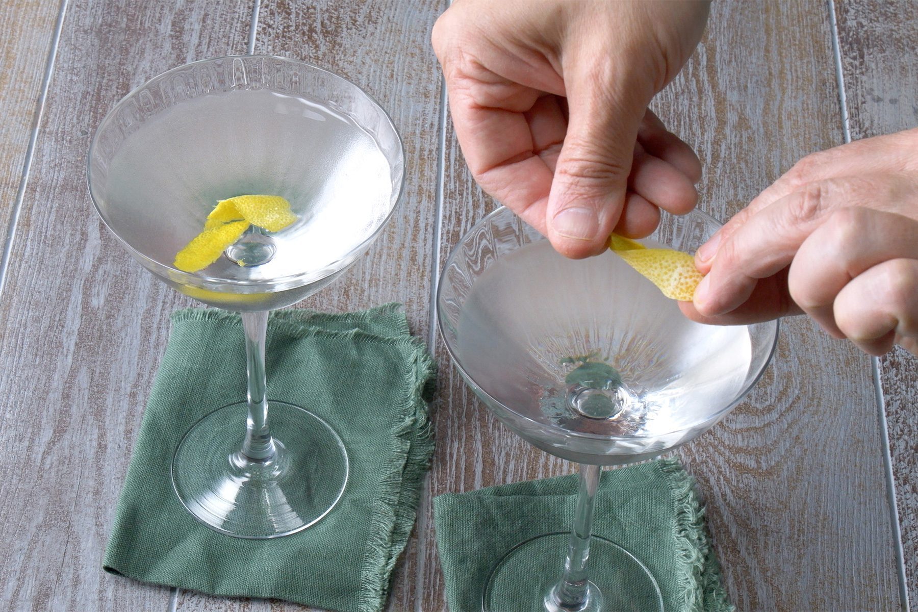 3/4th shot; wooden background; adding lemon peel in Vesper Martini drink; placed over green kitchen cloth;