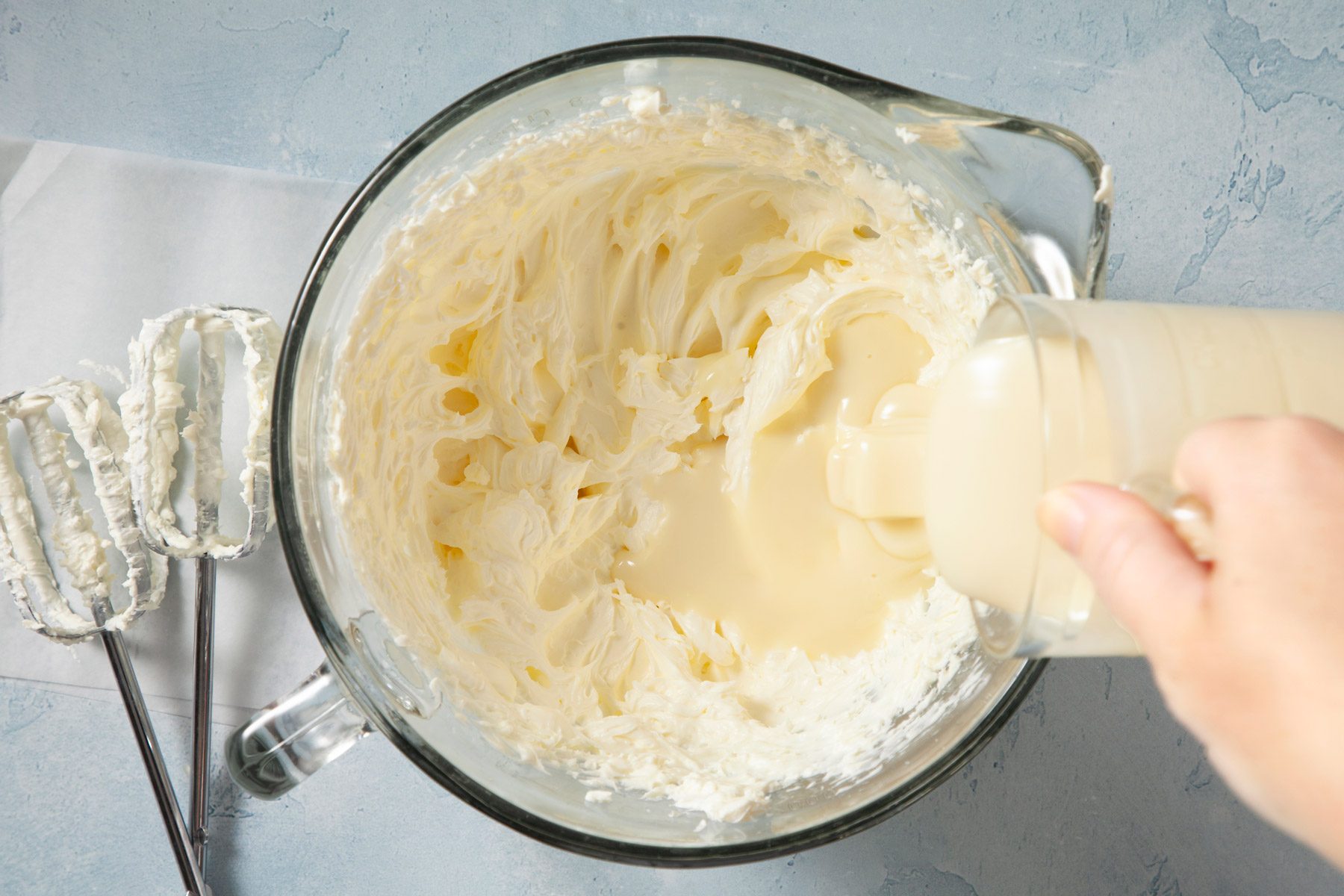 Sweetened condensed milk is being added to whipped cream.