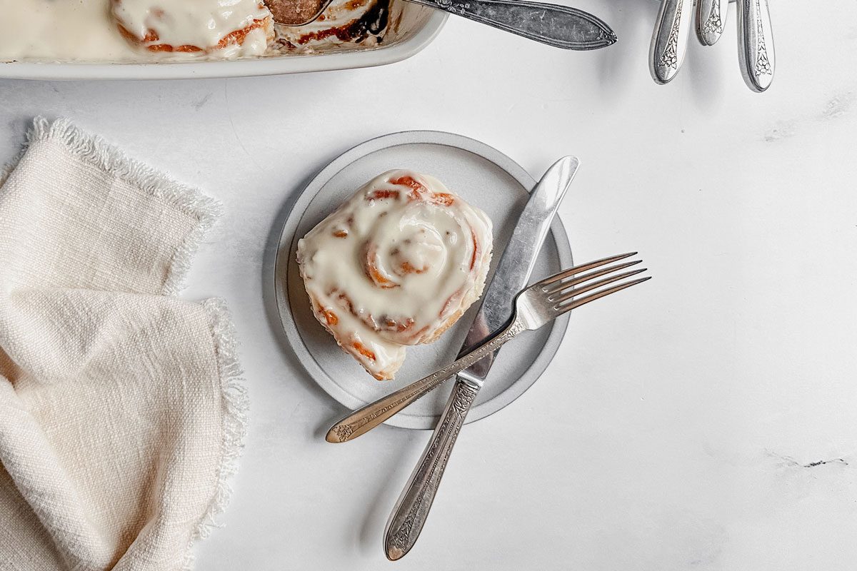 Taste of Home apple cinnamon roll on a white plate next to a cloth napkin on a marble surface.