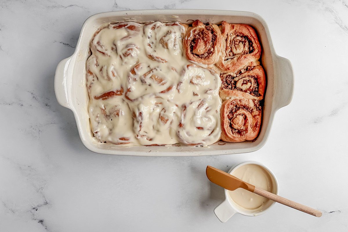 Taste of Home apple cinnamon rolls in a white baking dish spread with cream cheese frosting.