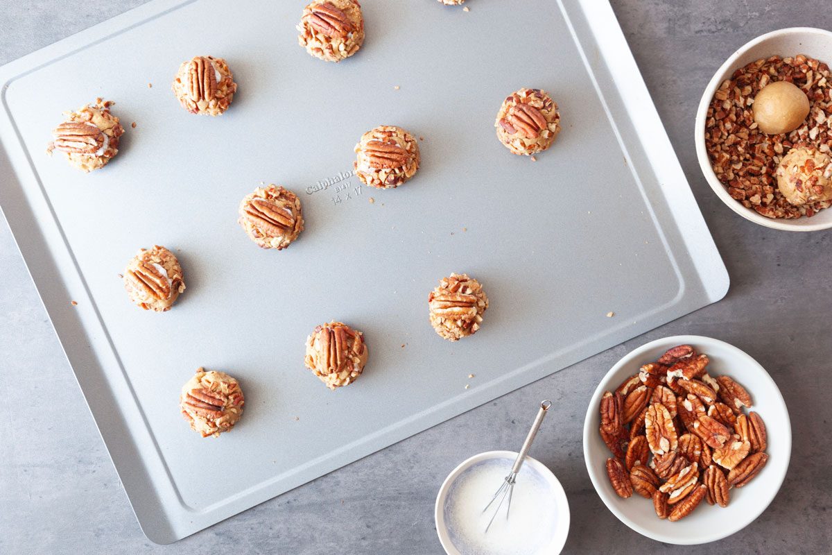 Step 3 of Taste of Home Butter Pecan Cookies is to roll dough into 1-inch balls, then roll balls in the chopped and toasted pecans, pressing nuts gently into the dough. Place 2 inches apart on an ungreased baking sheet. Beat egg until white and foamy. Next, dip pecan halves into egg white, and then gently press one into each ball.