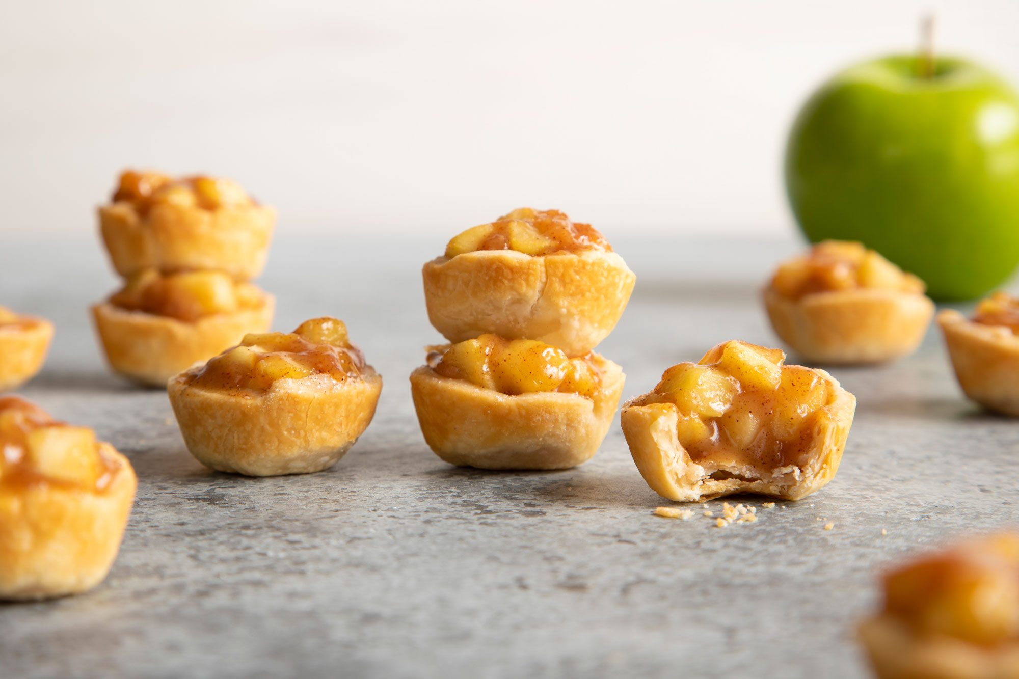 Caramel Apple Tartlets on grey background; green apple in the background;