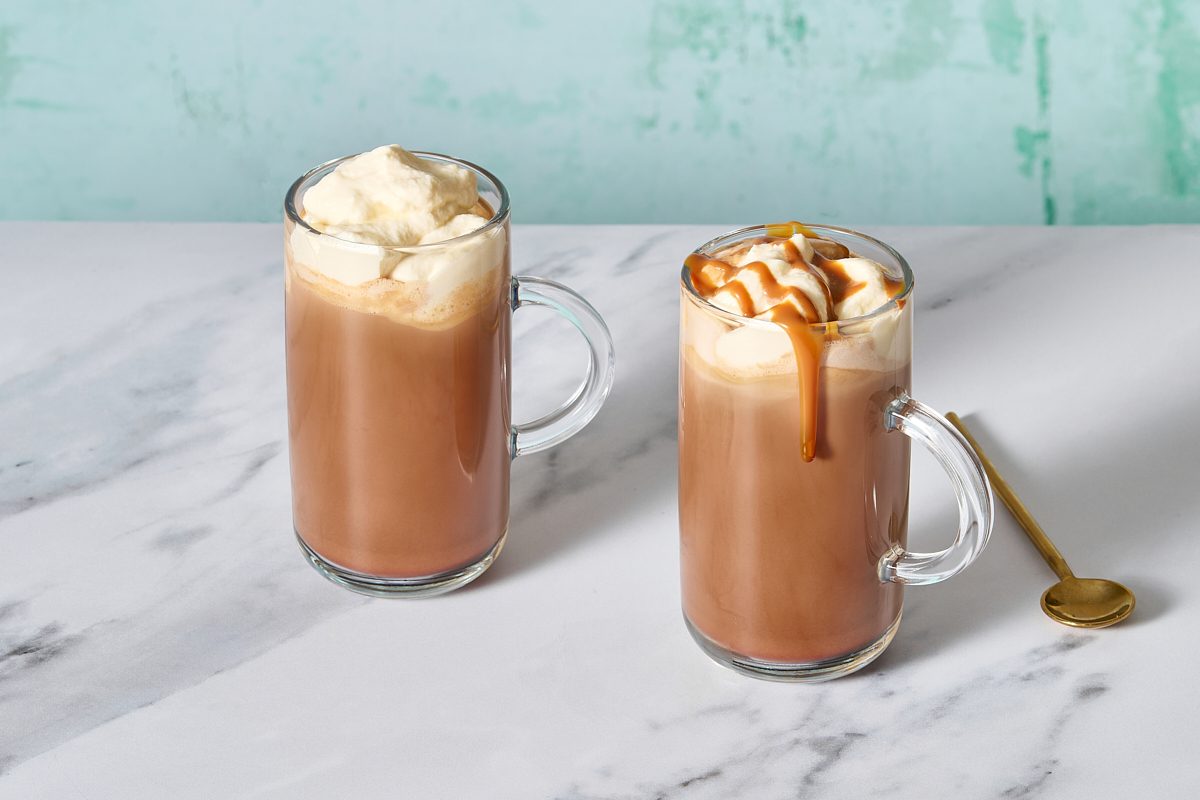 Two glass mugs of caramel mocha, topped with whipped cream and caramel drizzle