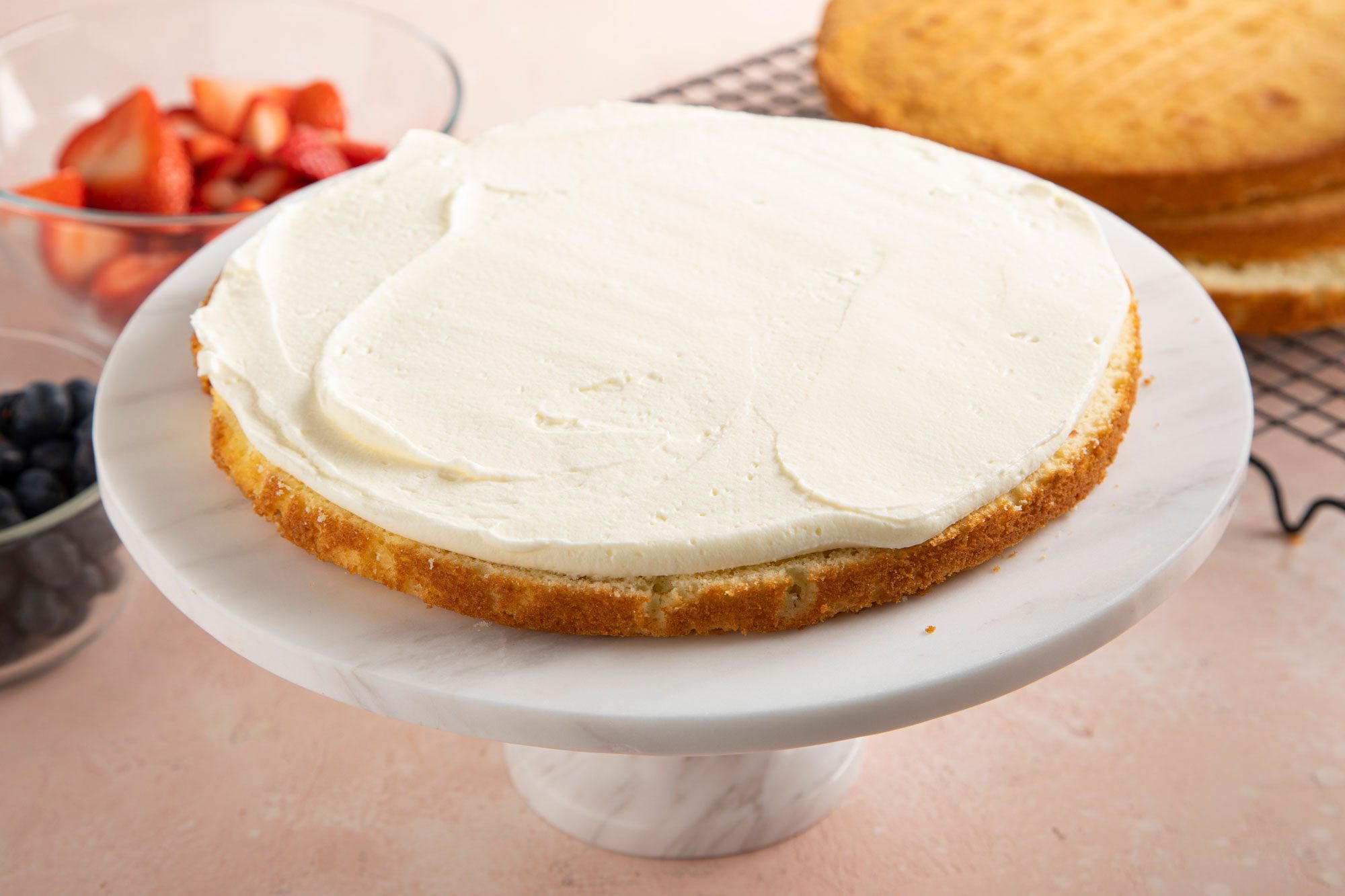 A round cake layer on a white marble cake stand, with a spread of frosting on top.