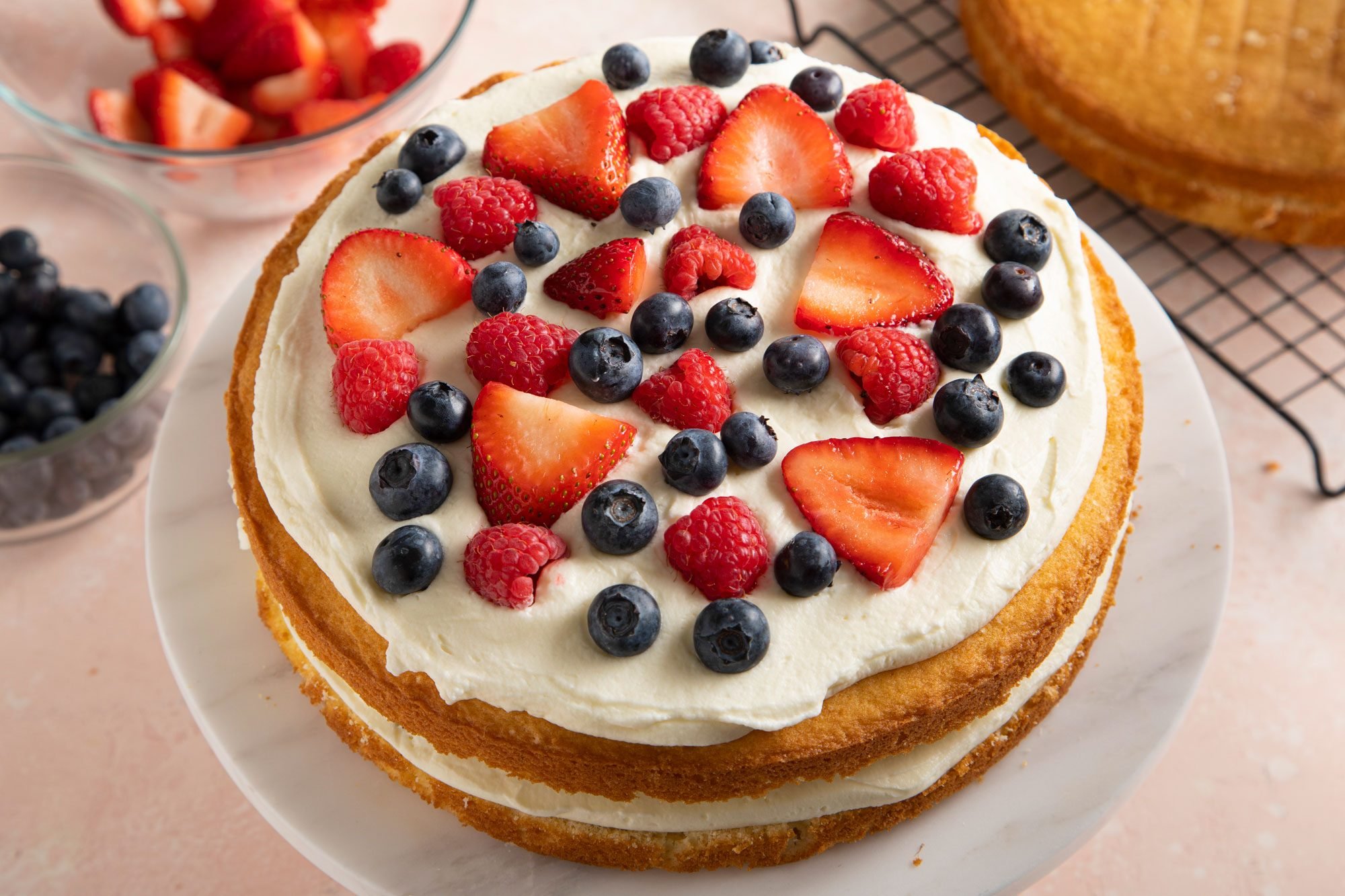 round cake layers on a white marble cake stand, with a spread of frosting, strawberries and blueberries on top.