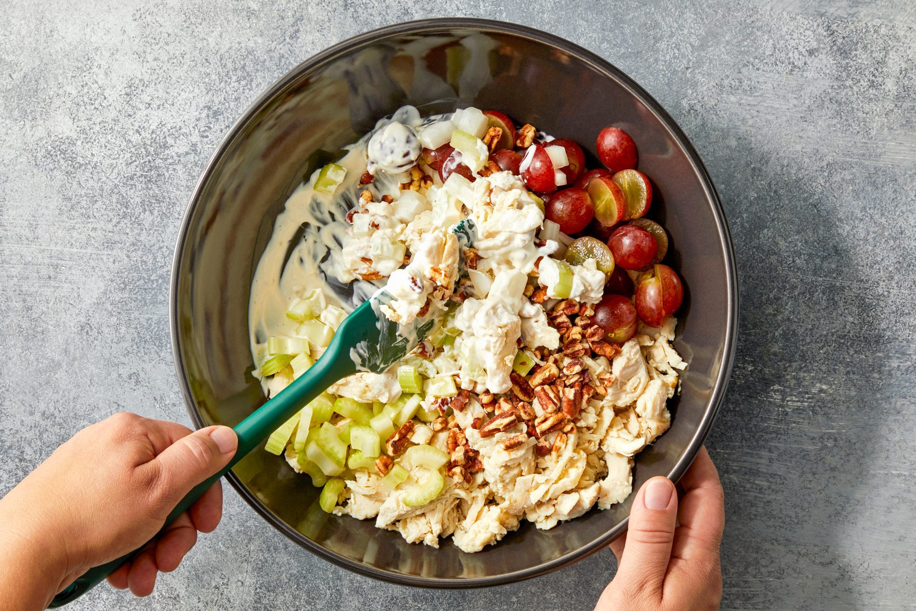 Chicken, grapes, pecans, celery and onions being mixed in a large bowl.