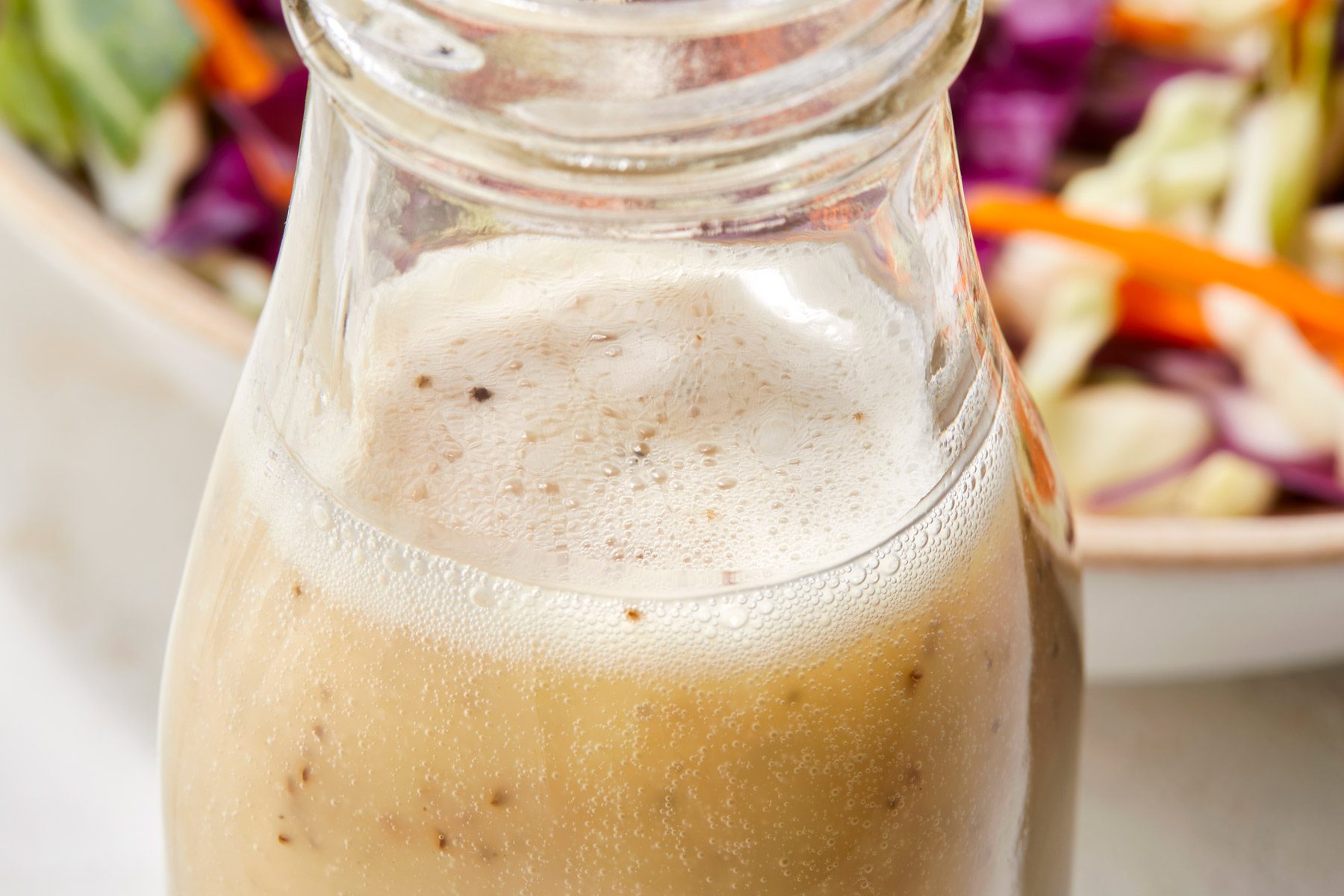 close up image of glass bottle containing coleslaw dressing. salad in a bowl can be seen in the background