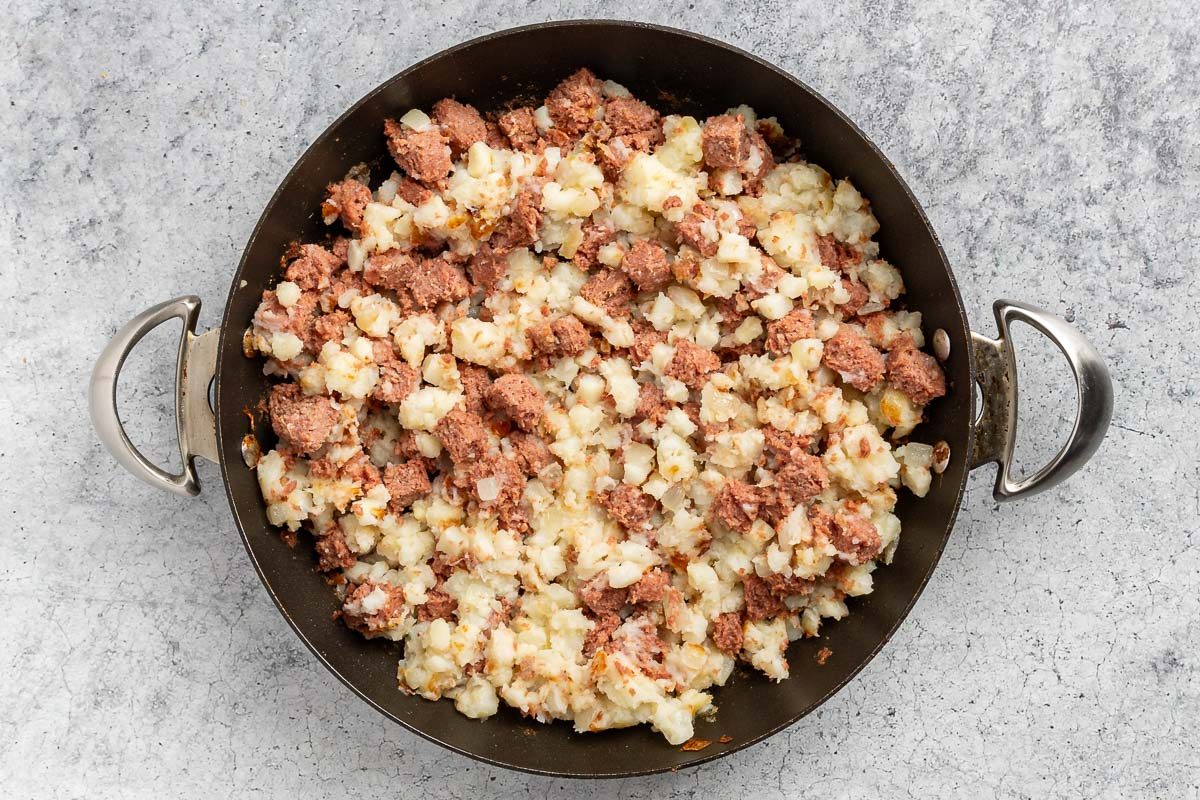 Taste Recipes Corned Beef Hash and Eggs recipe photo of the cooked potatoes, onions and corned beef in a skillet.