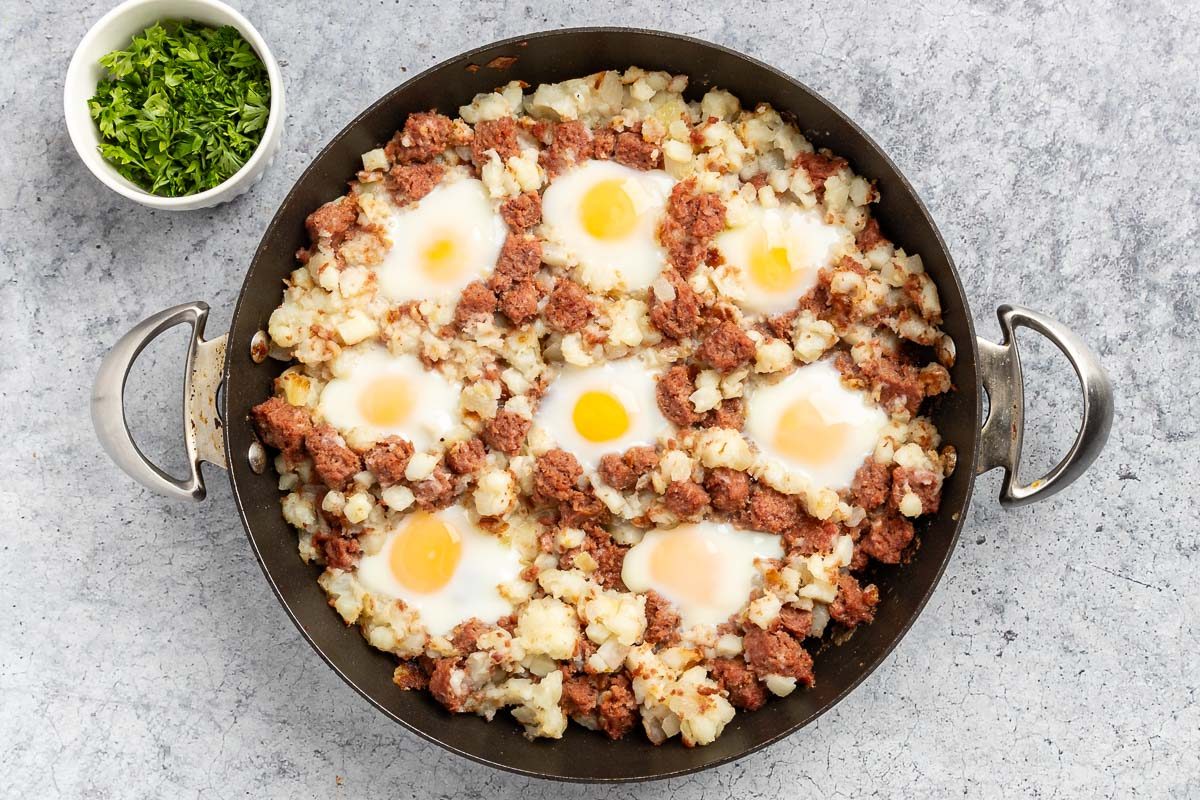 Taste Recipes Corned Beef Hash and Eggs recipe photo of the eggs added to the skillet, cooked and served with a garnish of parsley.