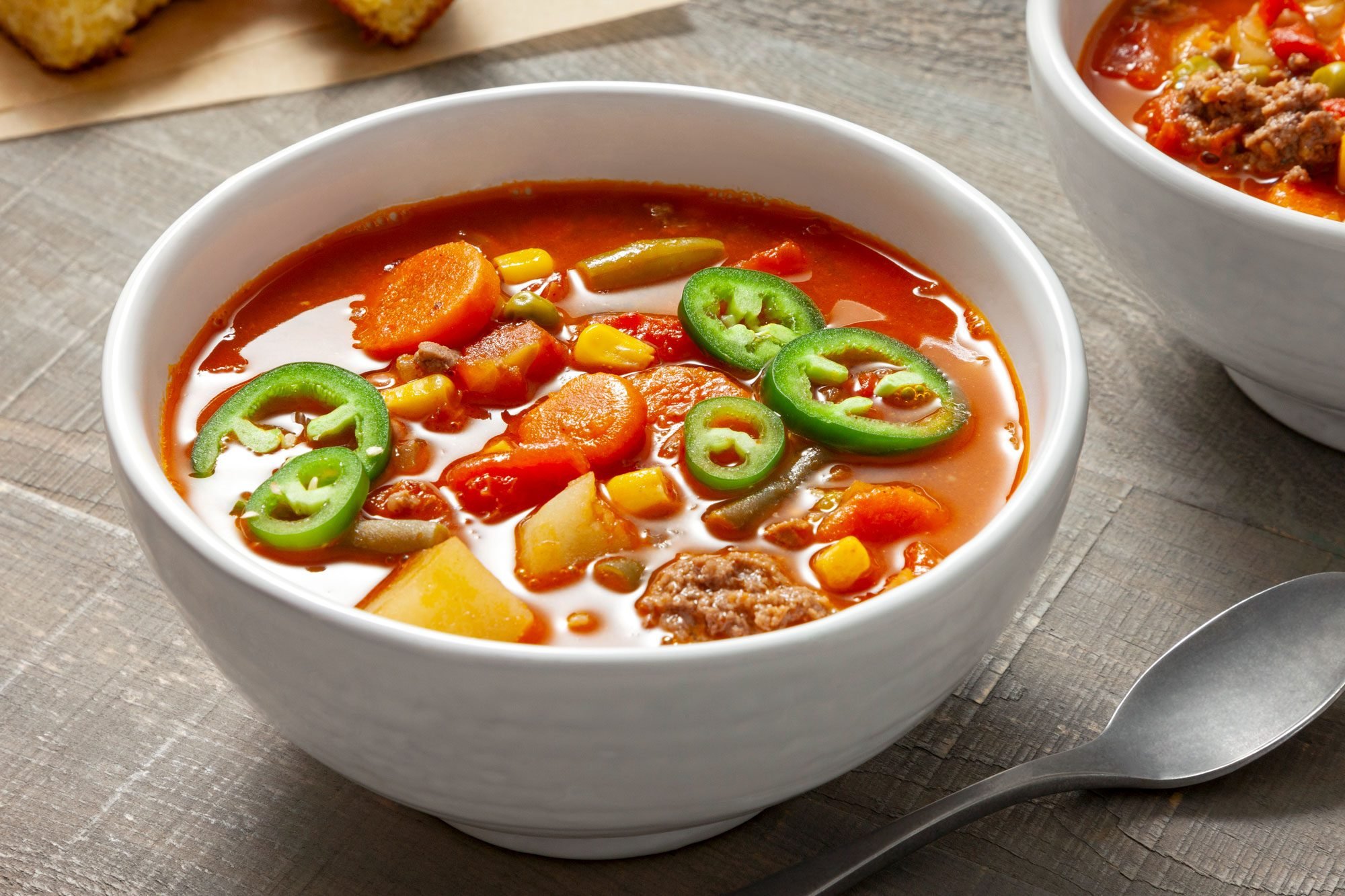 A white bowl filled with a cowboy soup; Another bowl of soup is partially visible; wooden background;