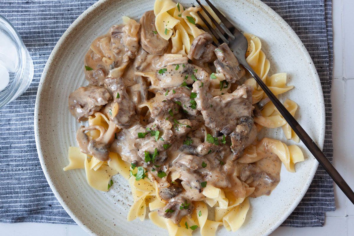 Close up of single serving of Taste of Home Crockpot Beef Stroganoff with egg noodles and garnished with parsley