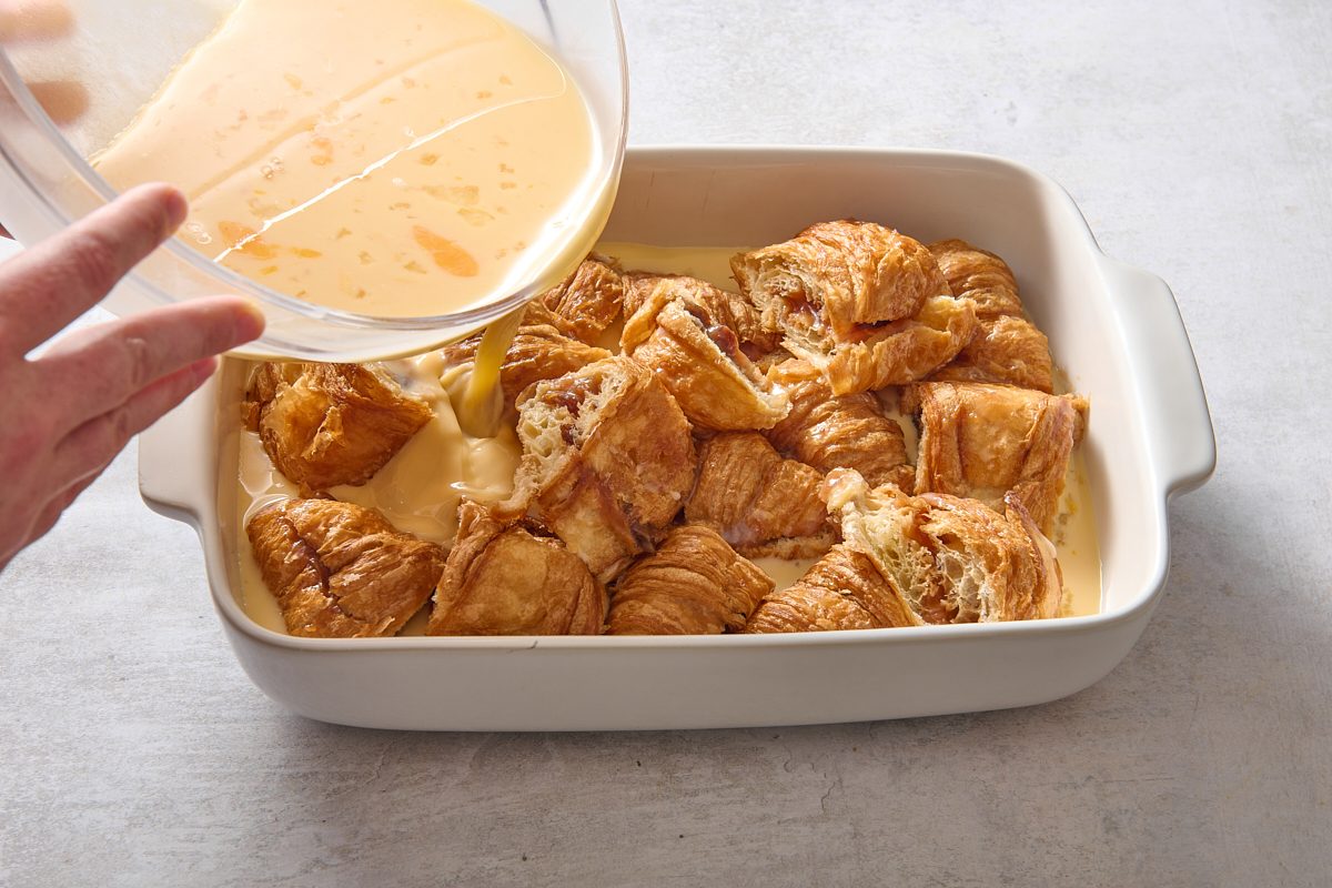 Pouring custard over the croissants in a baking dish