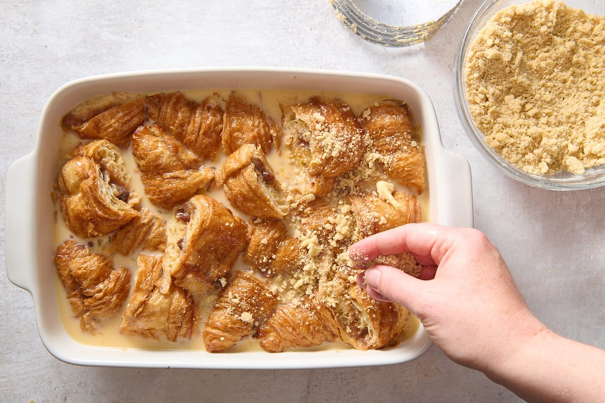 Sprinkling streusel topping over the croissant bake