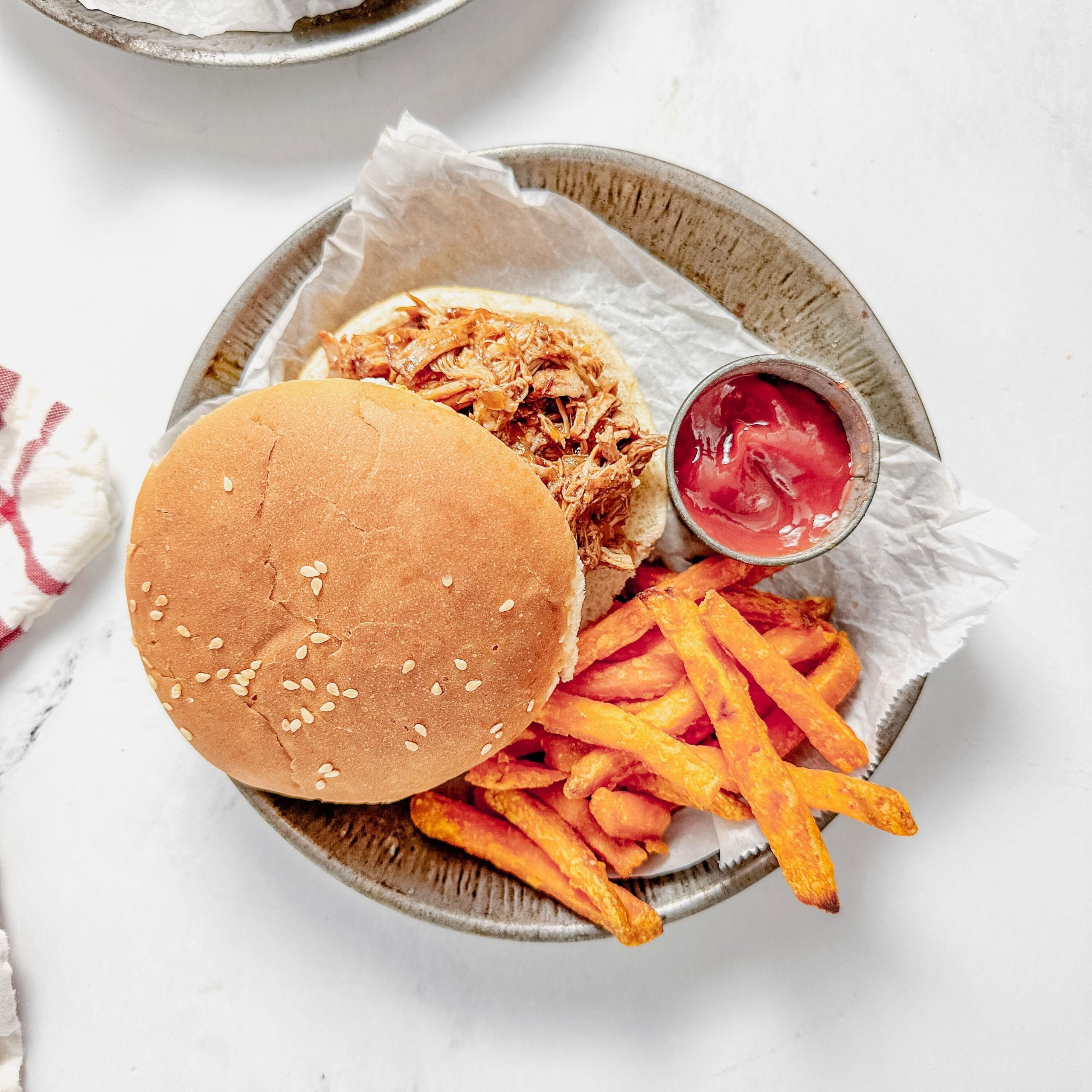 Taste of Home Dutch oven pulled pork on a metal plate with sweet potato fries and tin of ketchup on a marble surface